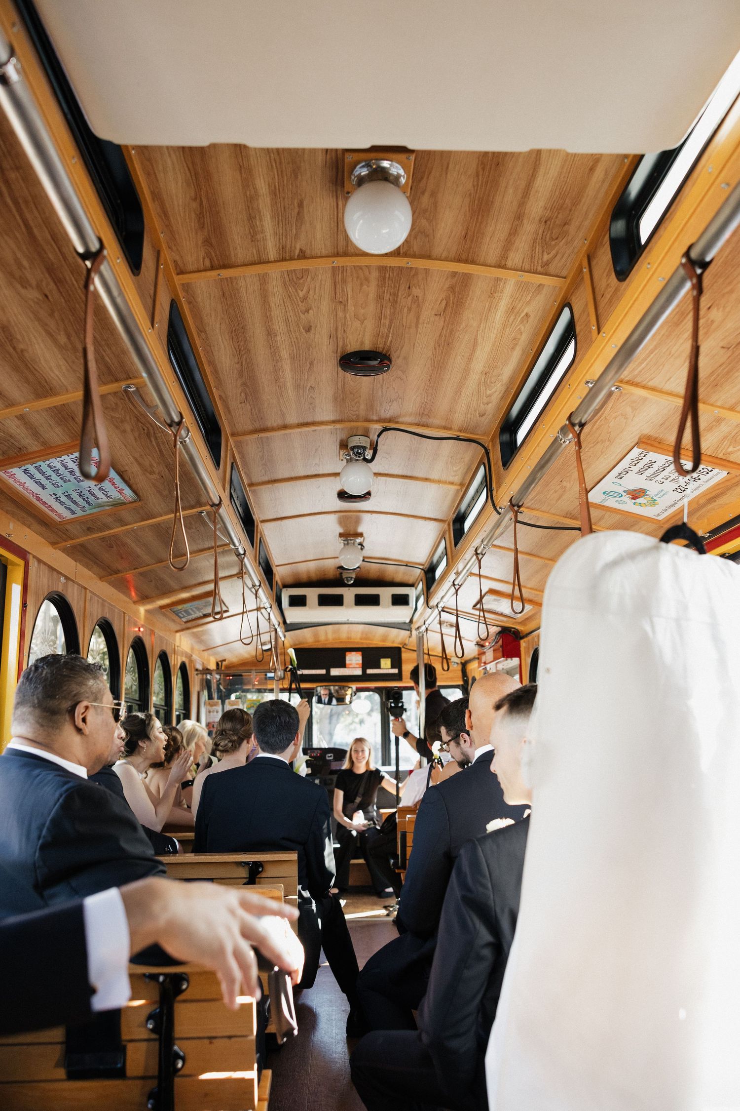 Interior view of a wooden trolley car filled with passengers in formal attire during a special event or celebration.