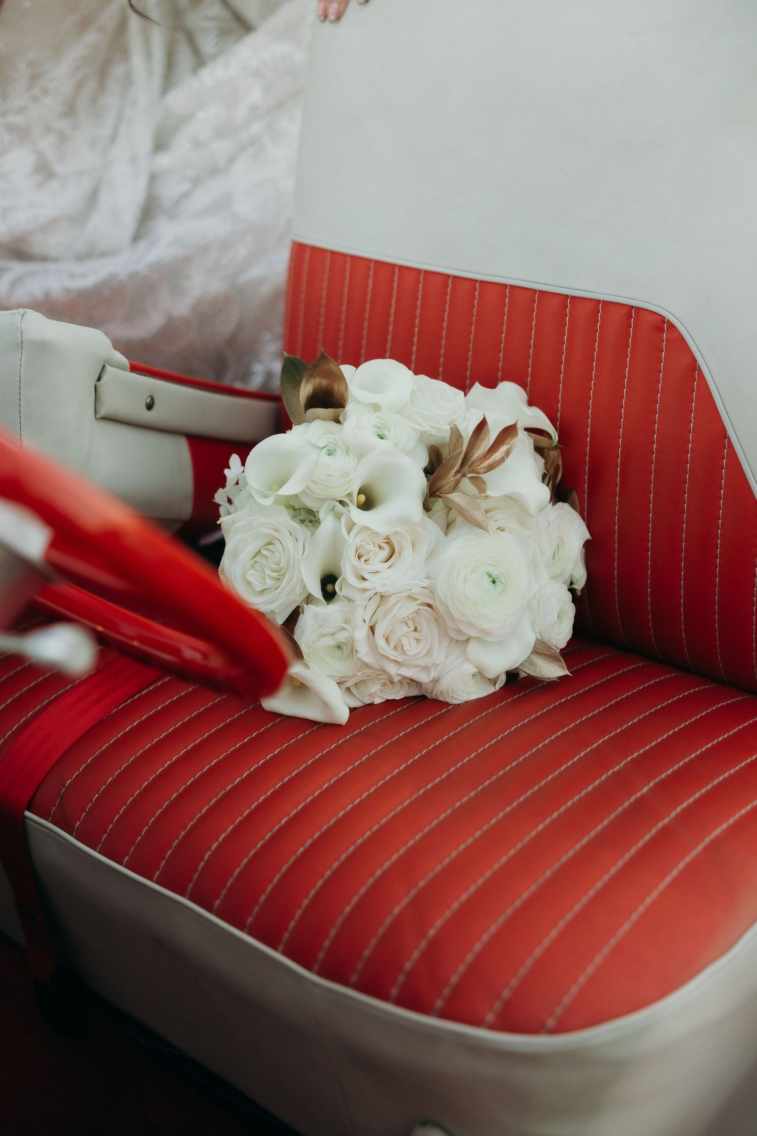 White roses resting on a vintage red leather car seat with pinstripe upholstery.