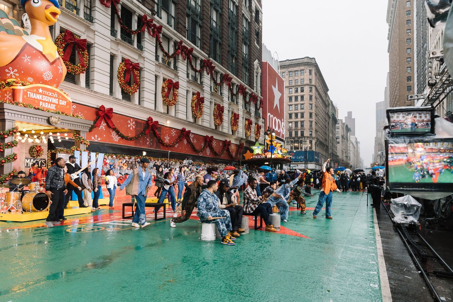 Rainy city street scene with green flooded pavement and buildings in the background.
