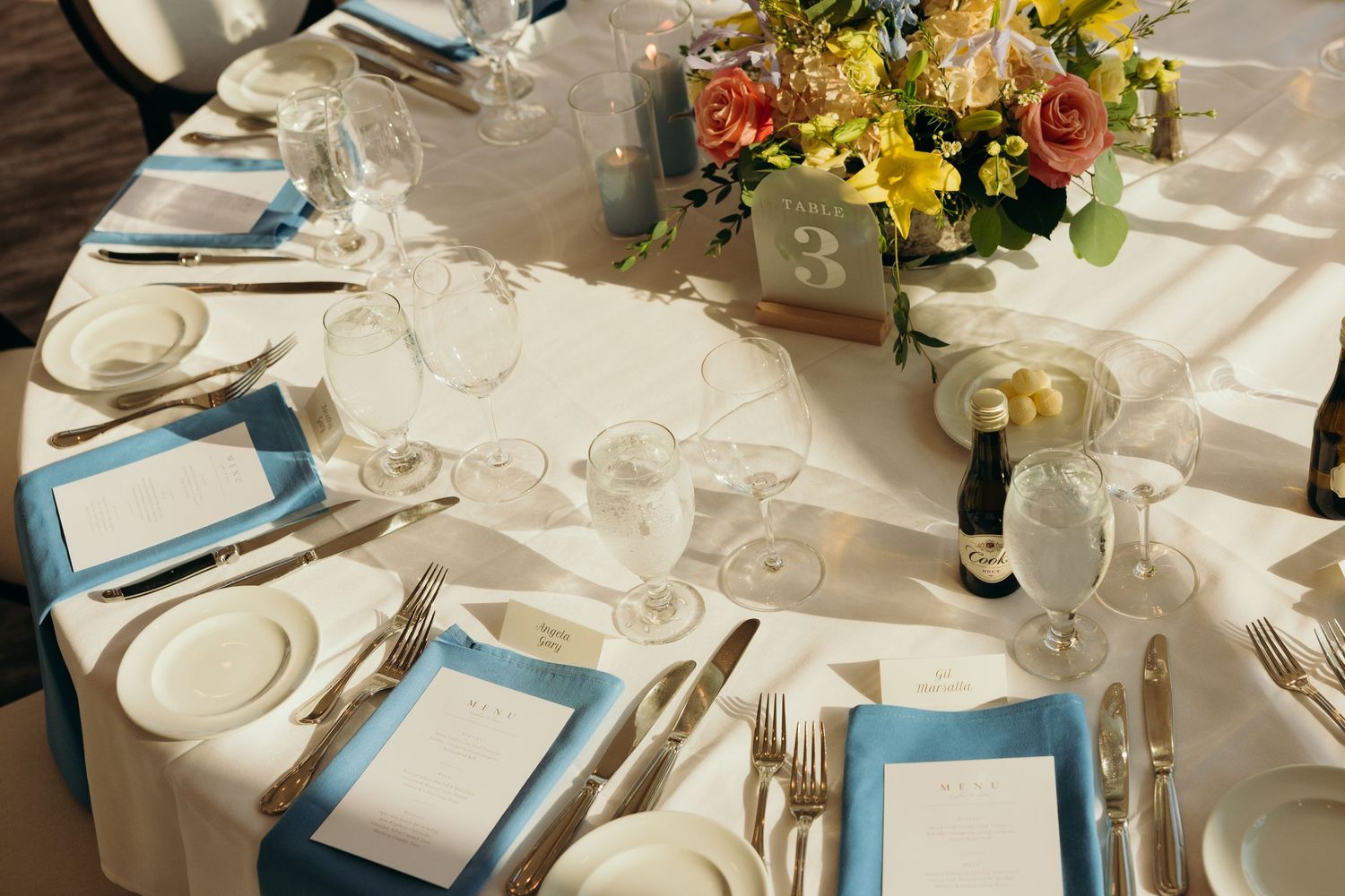 Elegant wedding reception tables decorated with white linens, blue accents, and floral centerpieces.