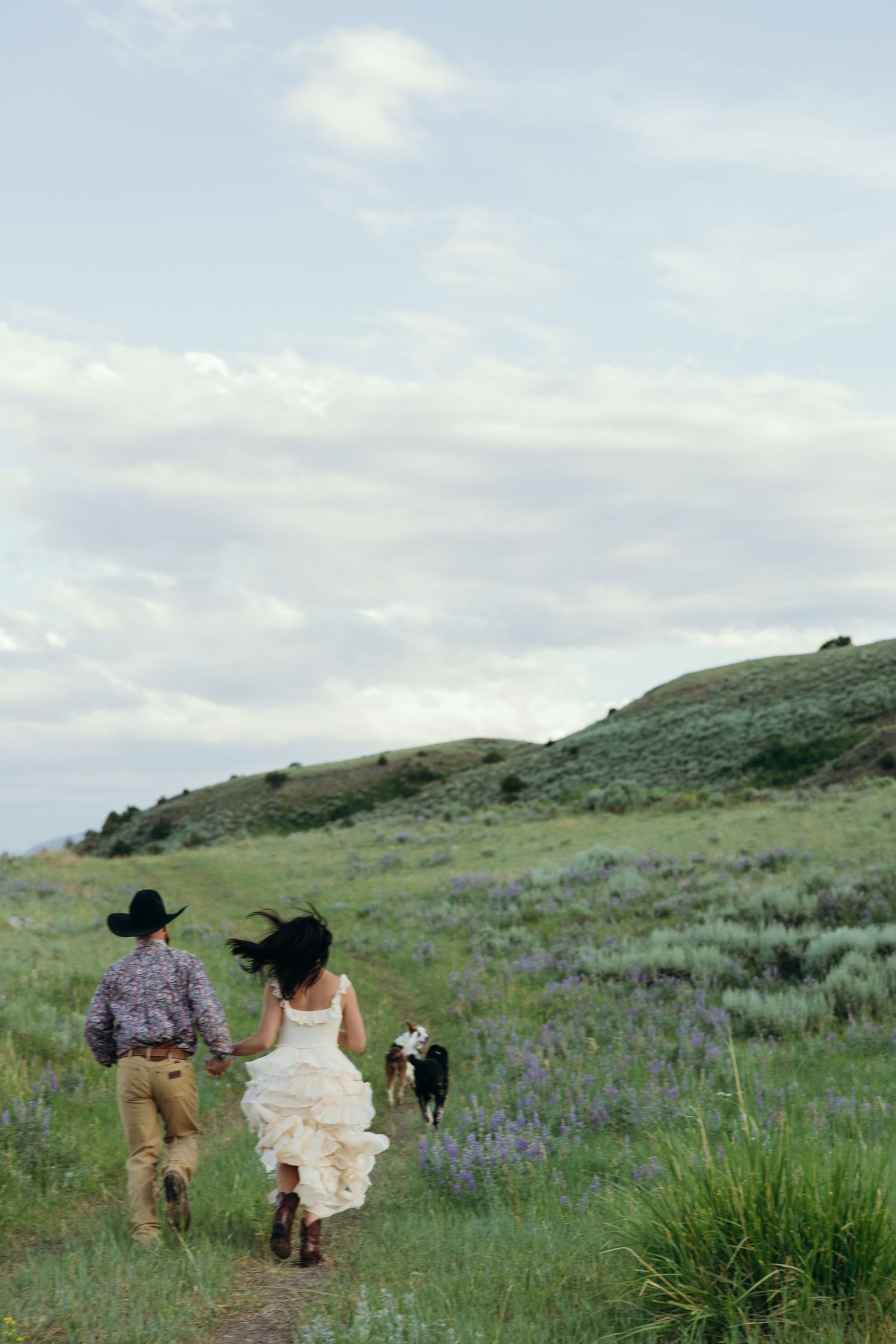 Two people walking through a wildflower-filled meadow with mountains in the distance.