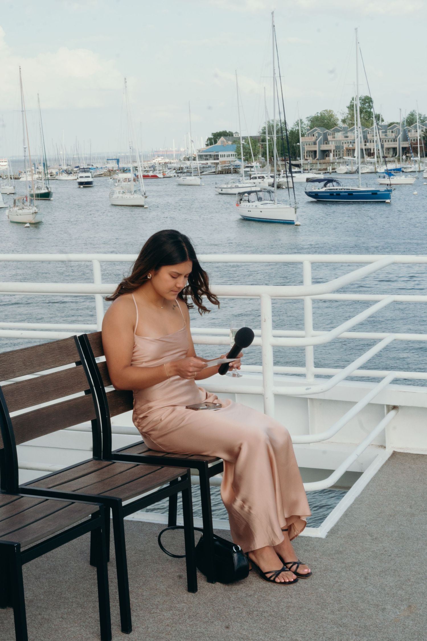 Person in a pink dress sitting on a bench at a marina looking at their phone.