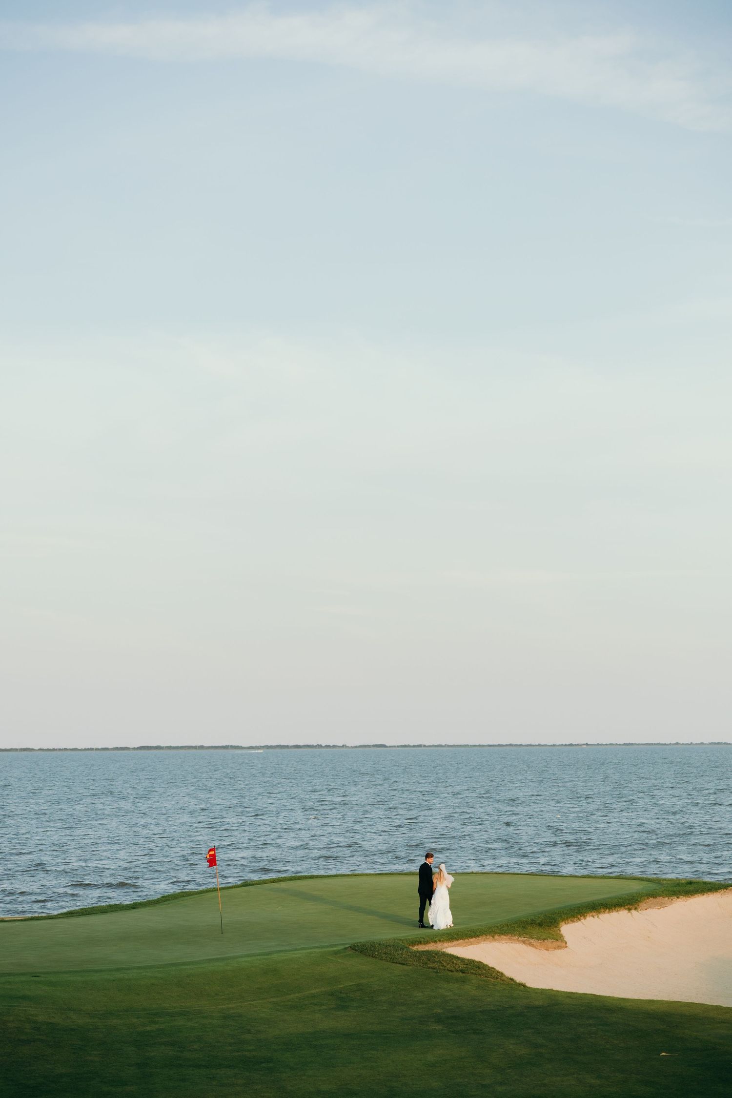 A couple stands on a coastal golf green with ocean views and sand trap.