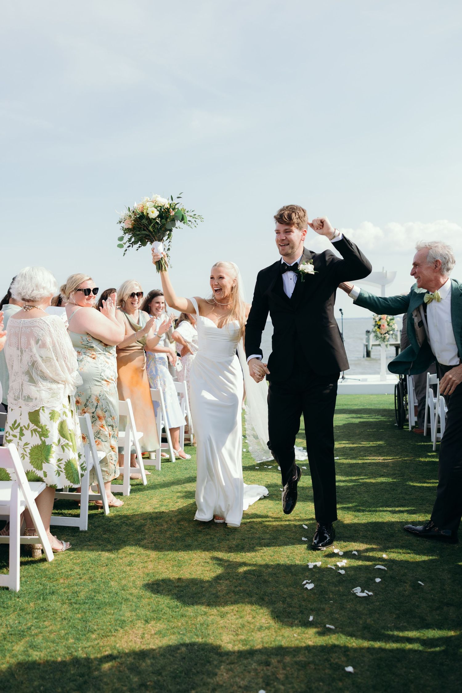 Wedding guests celebrate joyfully on a grassy lawn during the ceremony.