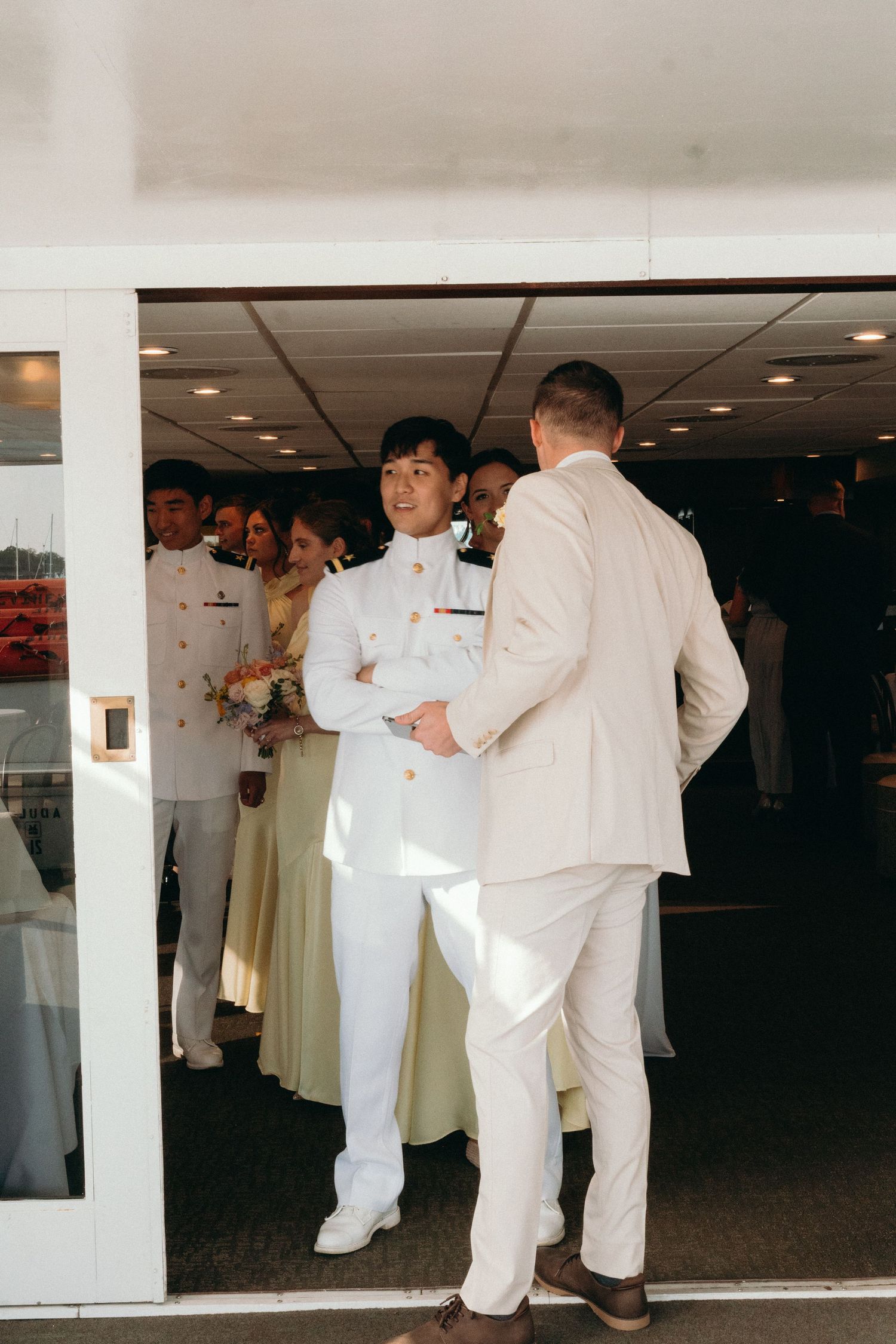 Wedding party members in white and beige formal attire mingling indoors.