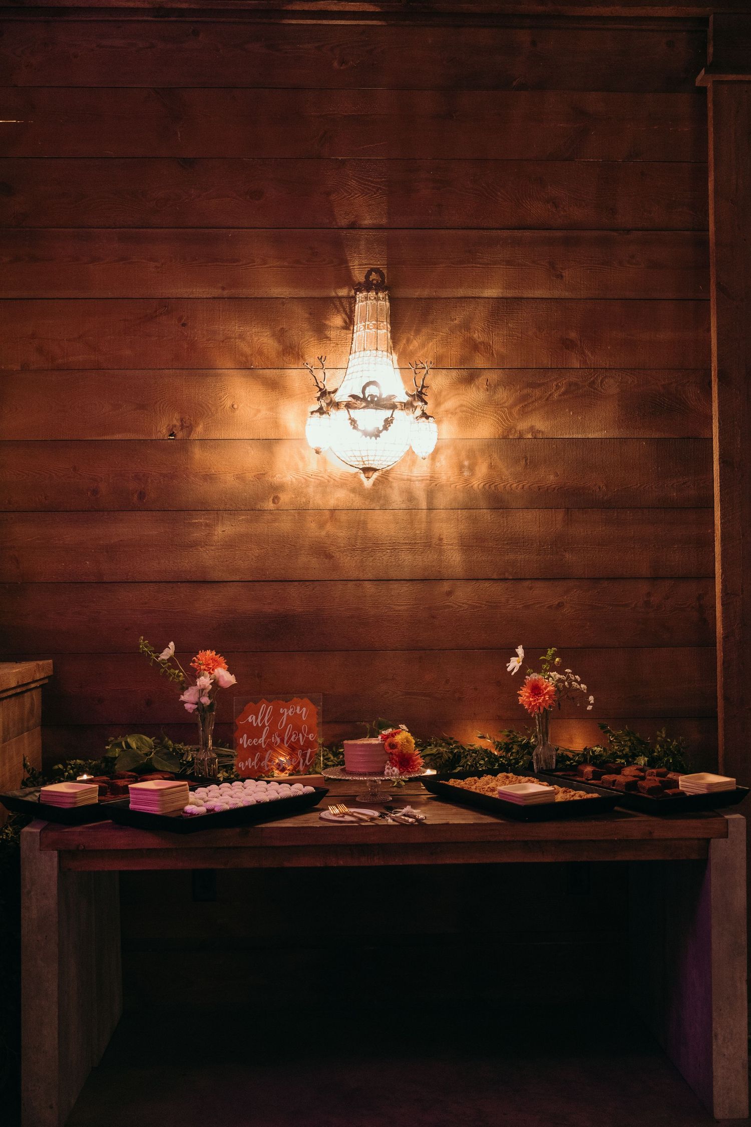 Rustic wooden wall with sconce lighting illuminates a buffet table decorated with various dishes and appetizers.