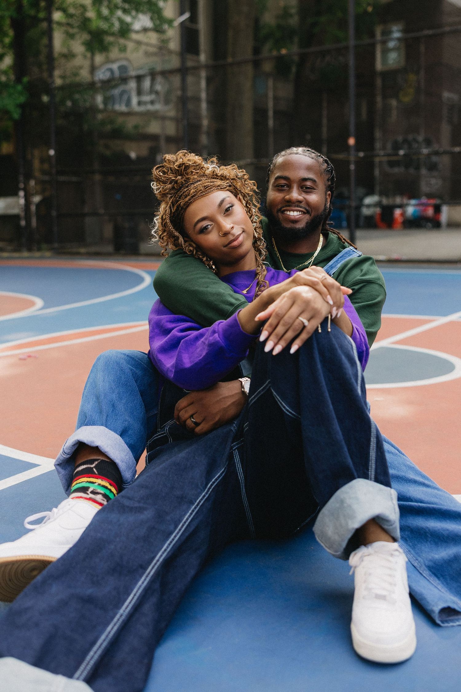 A couple in casual attire shares an intimate moment on a basketball court.