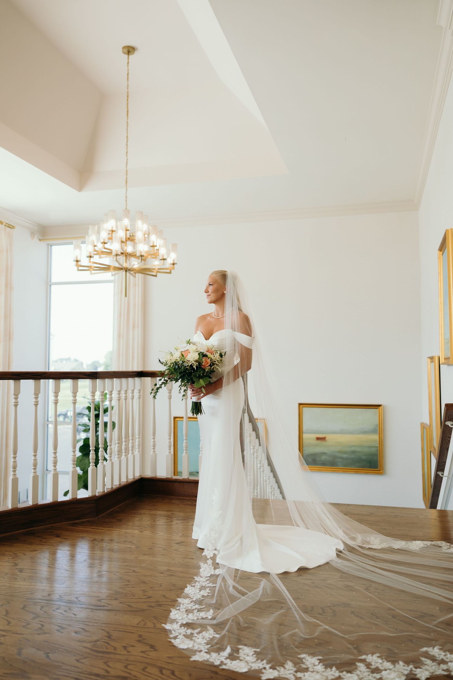 Elegant bridal portraits in white gown with long veil in sunlit room with chandelier.