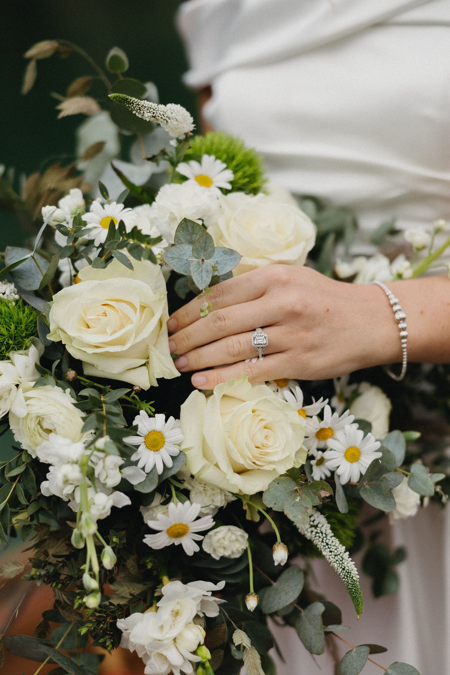 White and cream bridal bouquet featuring roses, daisies and eucalyptus with diamond ring detail.