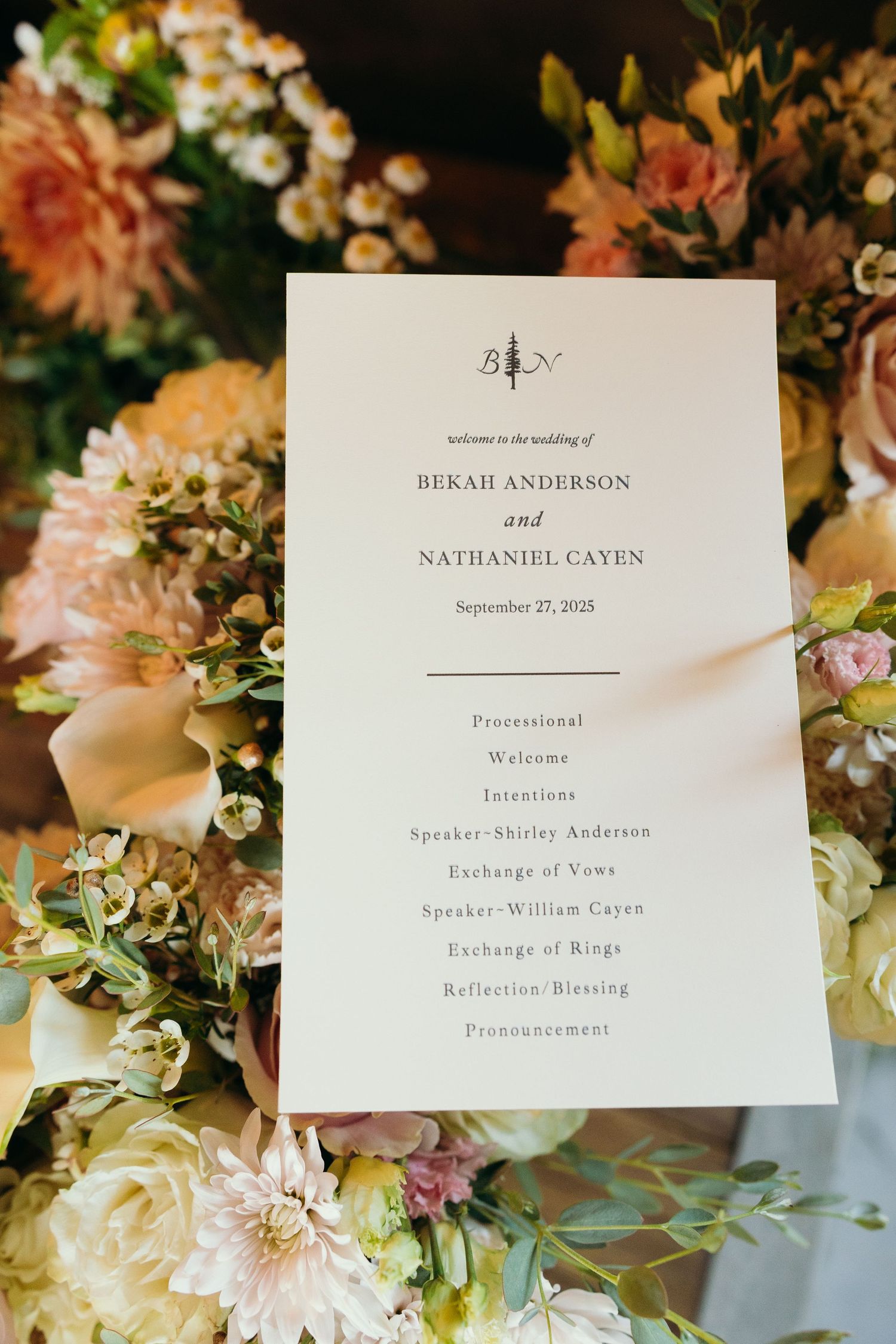 Wedding ceremony program and floral arrangements displayed on decorated table.