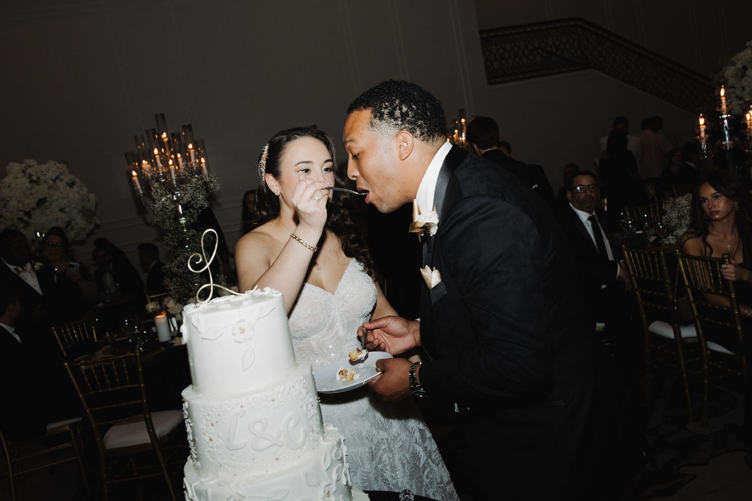 A couple shares their first dance at a dimly lit wedding reception surrounded by guests and candlelight.