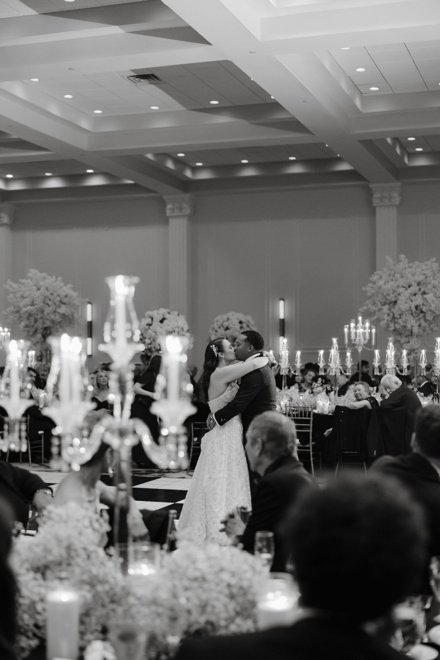 A romantic candlelit reception with a couple dancing amidst elegant table settings and floral arrangements.