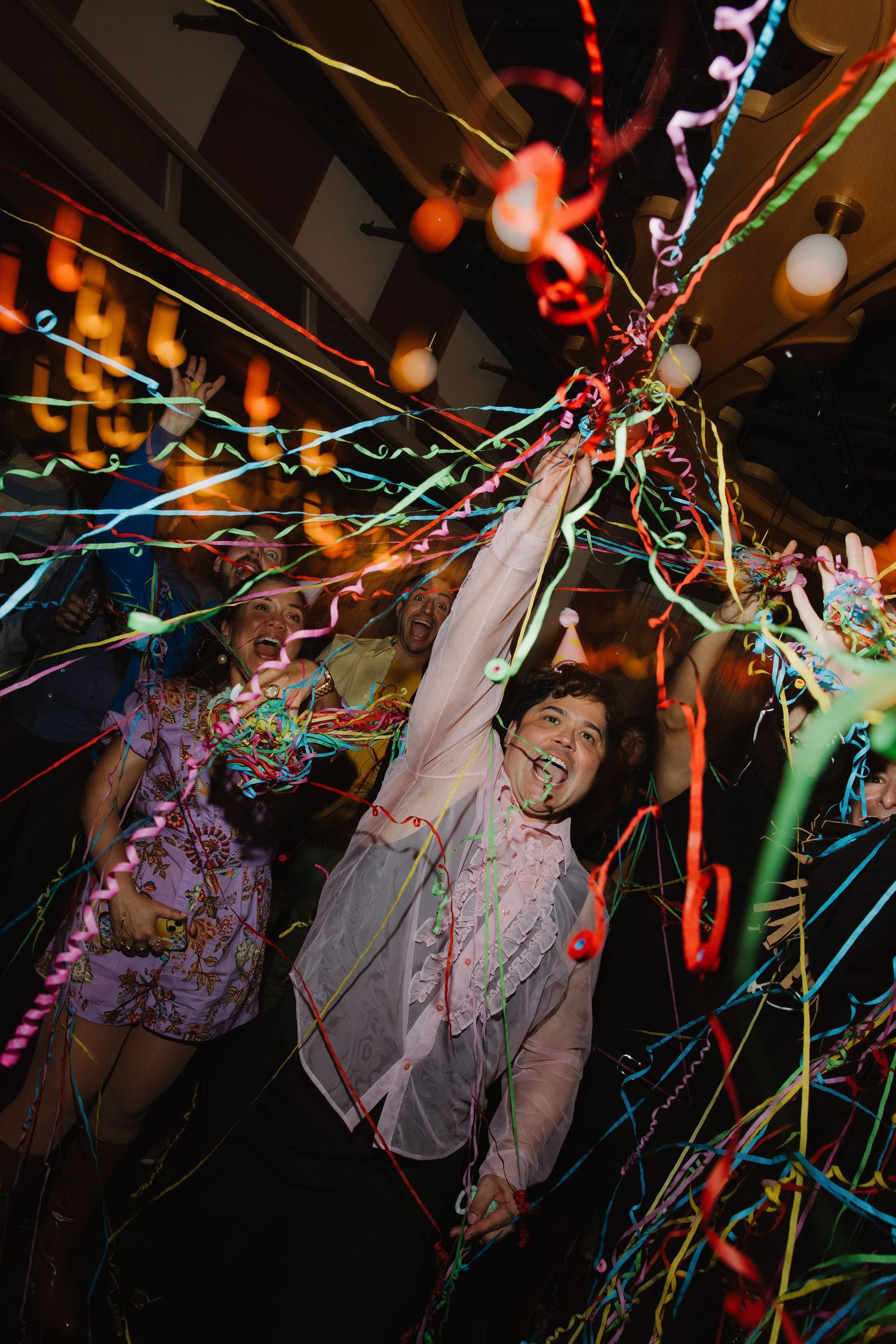 People celebrating at a party with colorful streamers and confetti flying through the air.