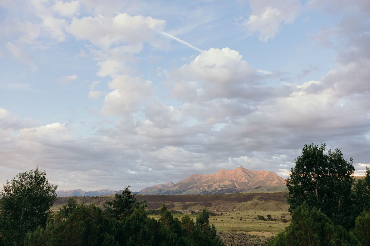 Panoramic landscape view of mountains and trees under a cloudy blue sky.
