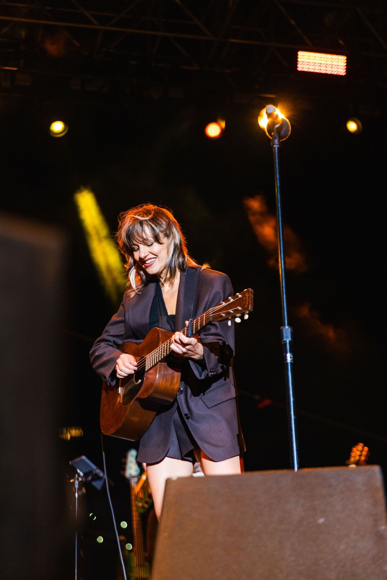 Anais Mitchell playing acoustic guitar on stage in dark lighting conditions.