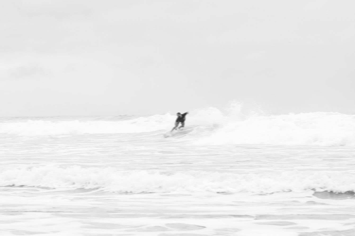 A surfer rides a large wave in the ocean as it breaks and creates white foam spray.