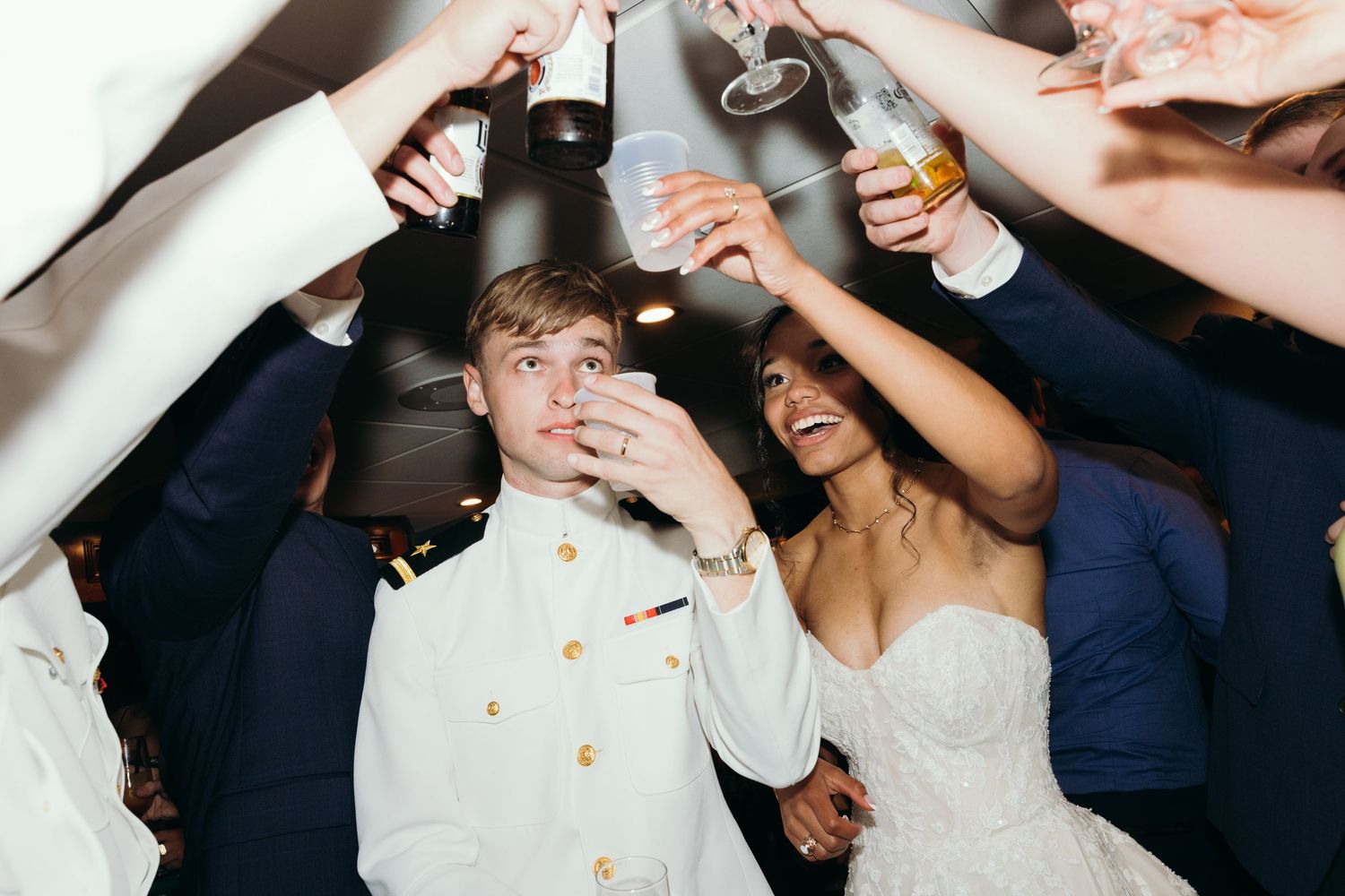 Wedding celebration with guests raising drinks and cheering around the newlyweds.