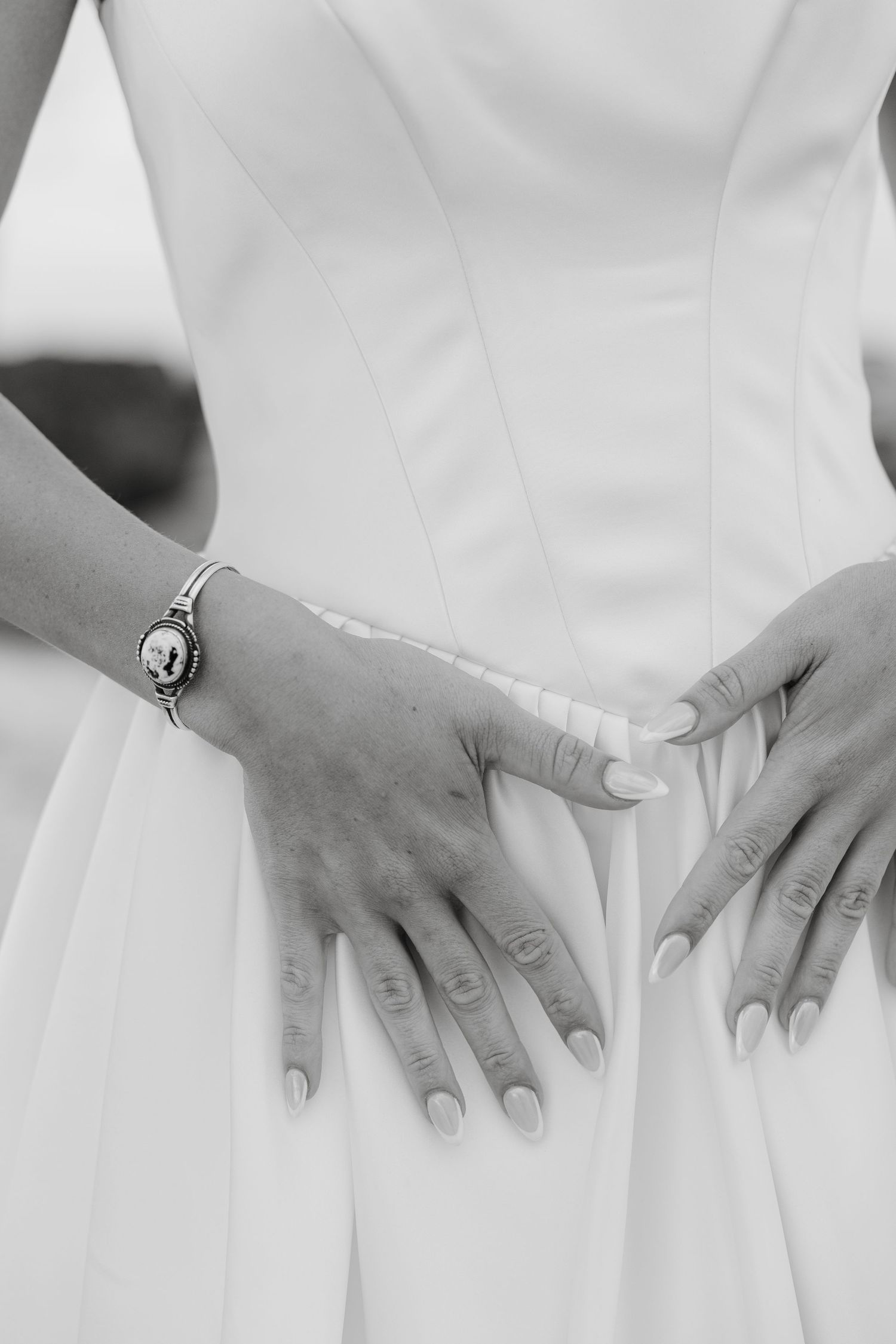 Close-up details of hands against white wedding dress showing elegant ring.