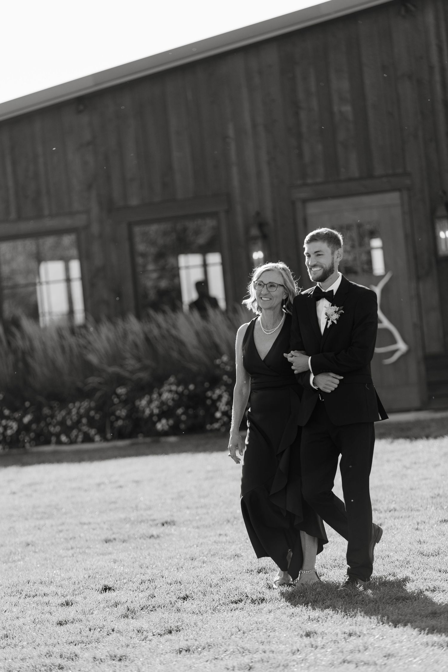 Black and white photo of a couple walking near a rustic barn.