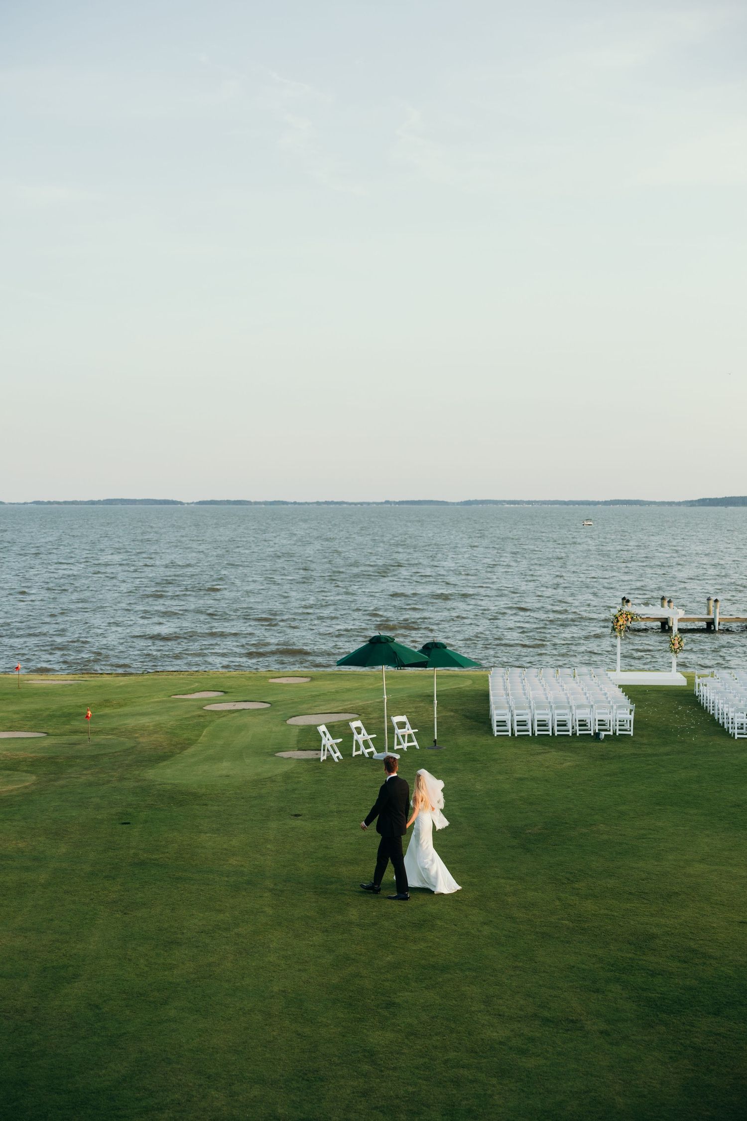 A wedding ceremony setup on a scenic waterfront lawn with white chairs and ocean views.