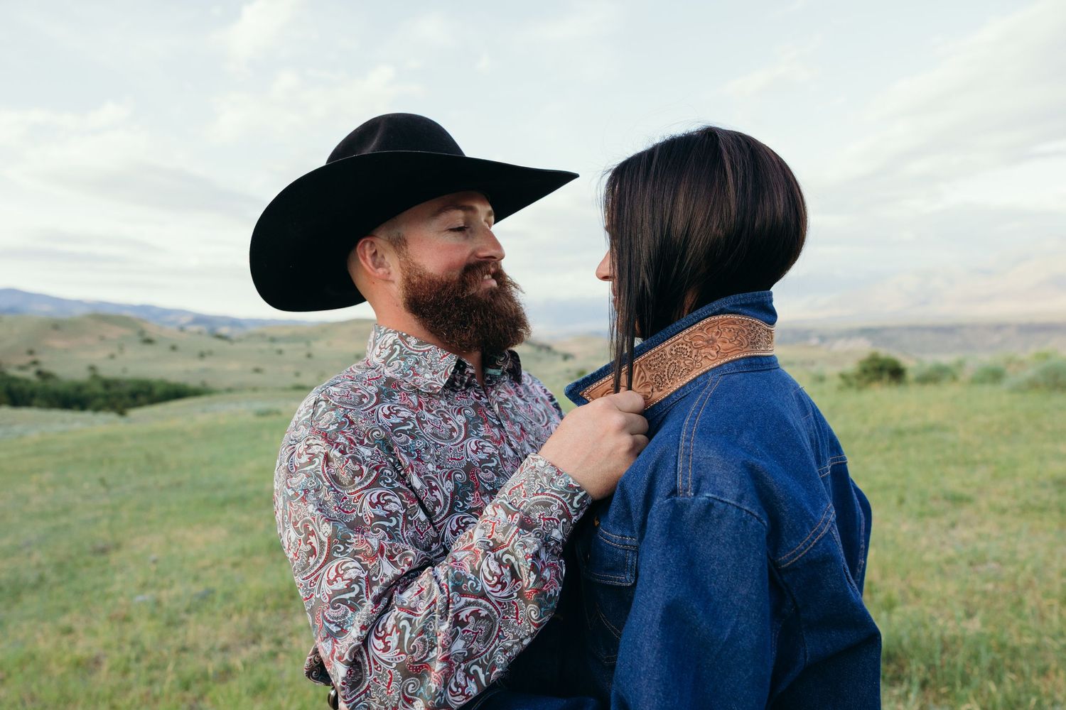 Intimate moment shared between two people wearing western hats in a mountain landscape.