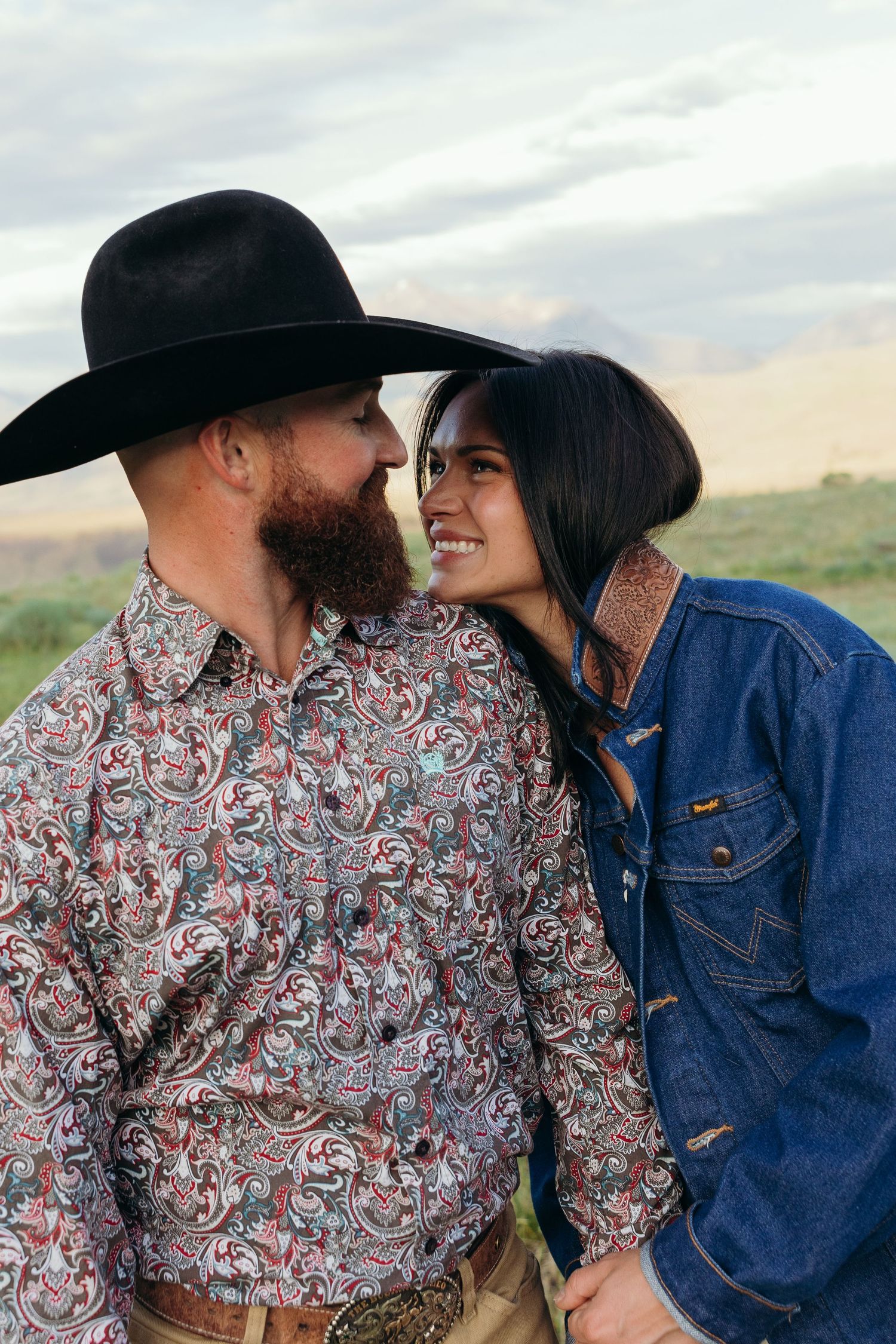 Couple in western wear sharing intimate moments with mountains visible in the background.