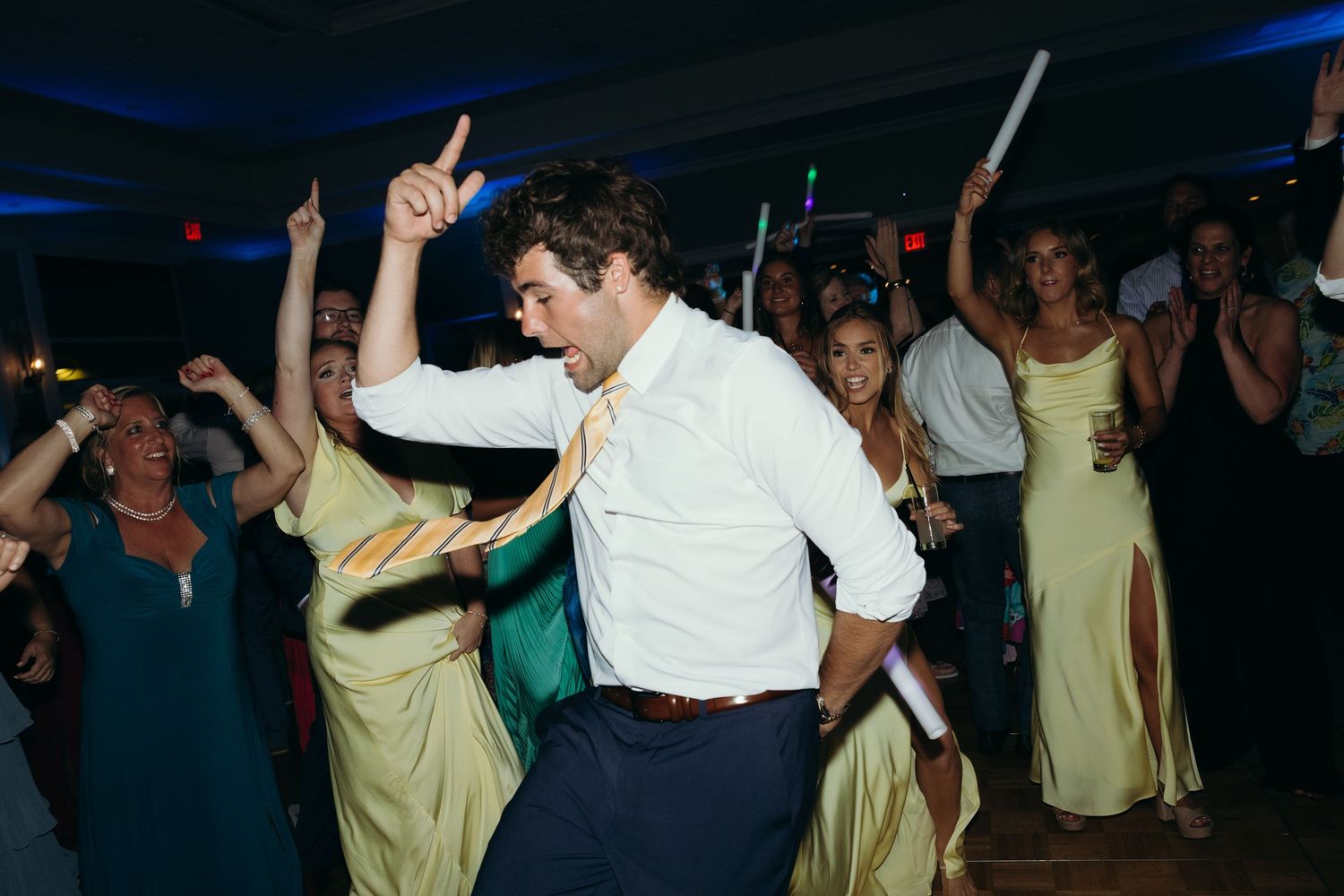 Party guests dancing and raising their hands on a dark dance floor with blue lighting.