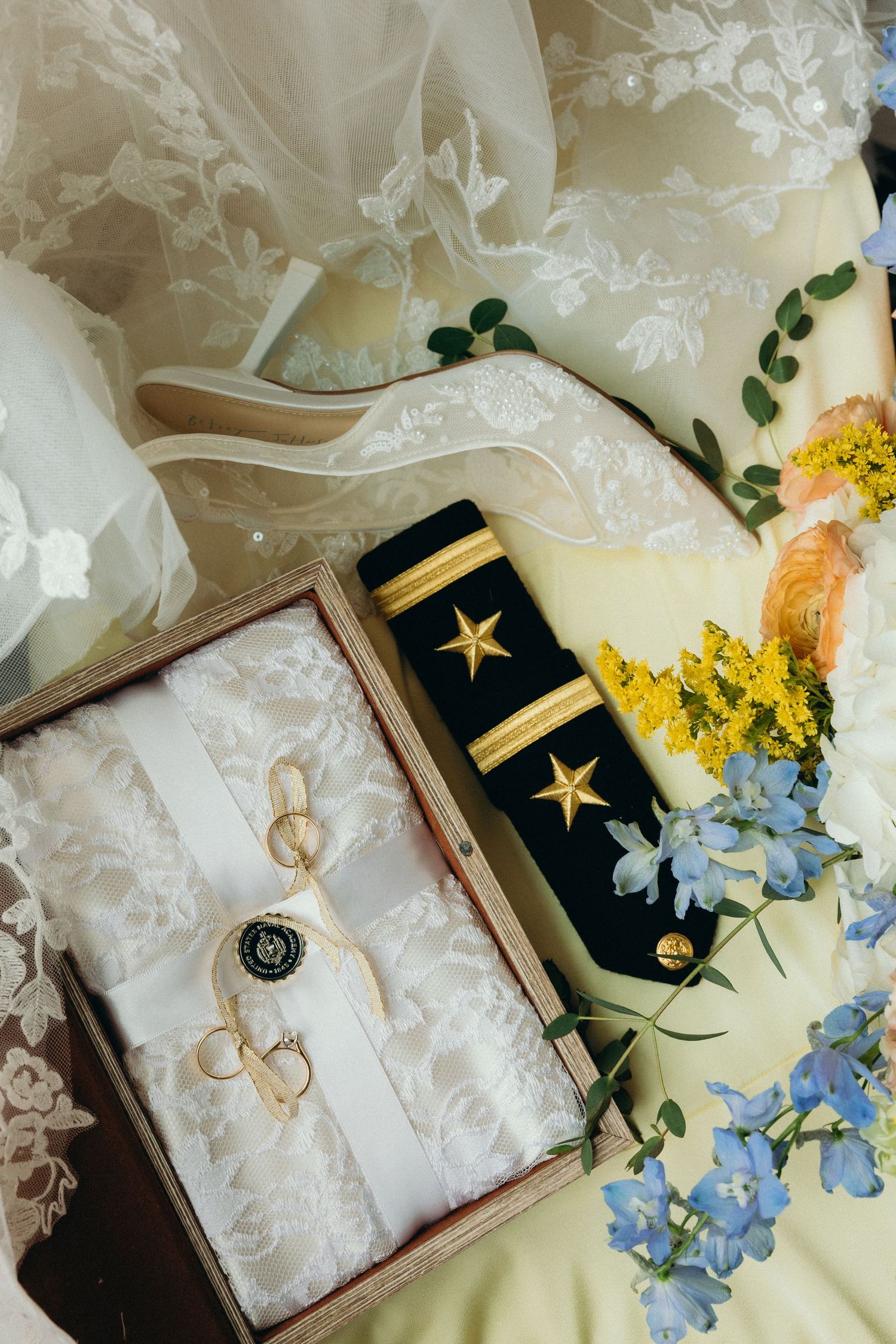 Military uniform epaulettes with gold stars displayed alongside delicate lace and blue flowers.