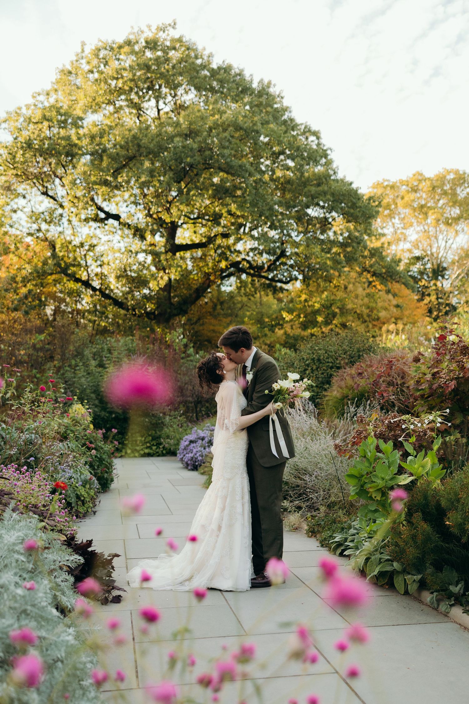 Couple dancing in a blooming garden path with pink cosmos flowers in foreground.
