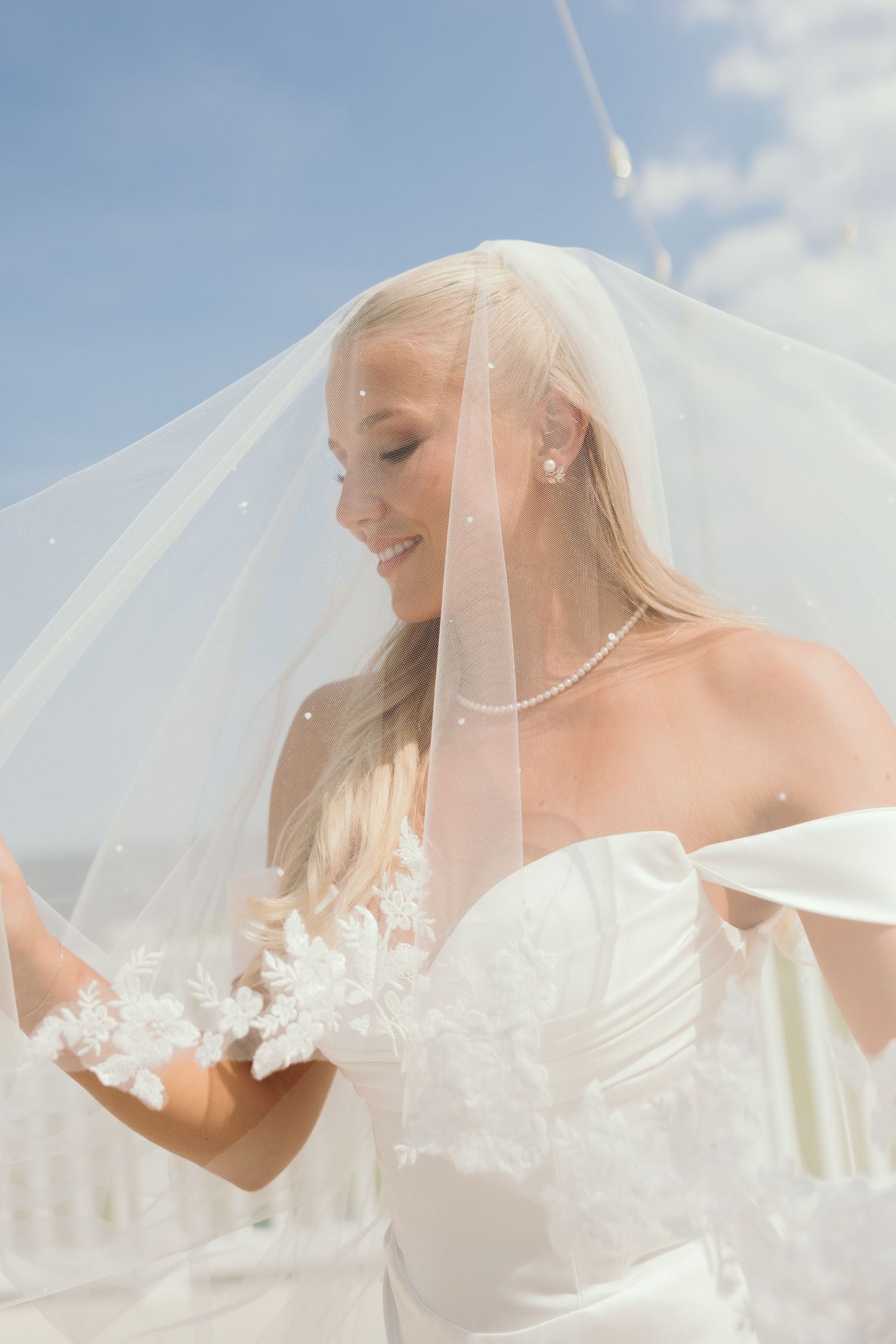 Ethereal bridal portrait showing flowing veil against blue sky.