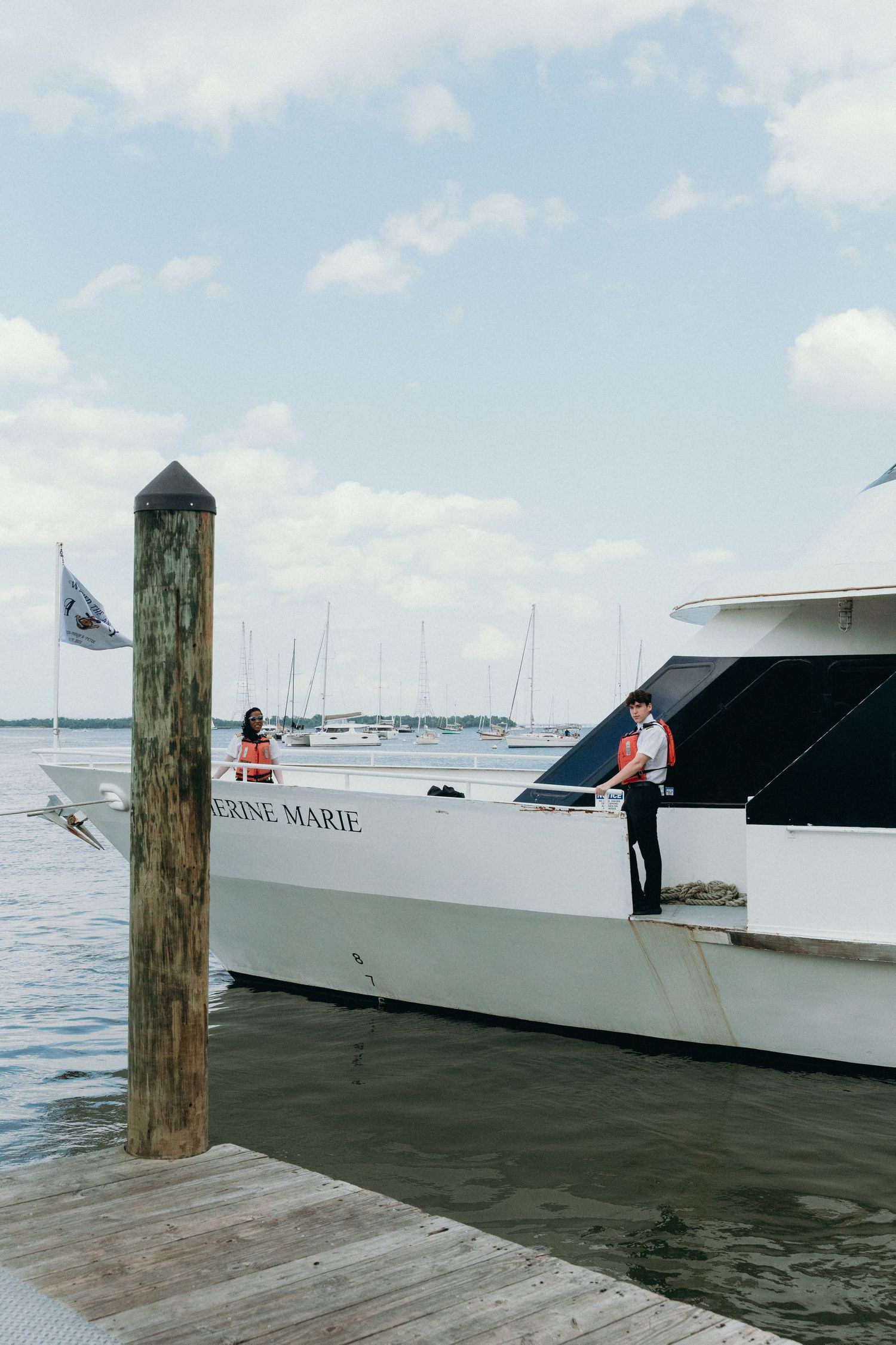 Large white yacht docked at a marina with wooden posts and other boats in the background.