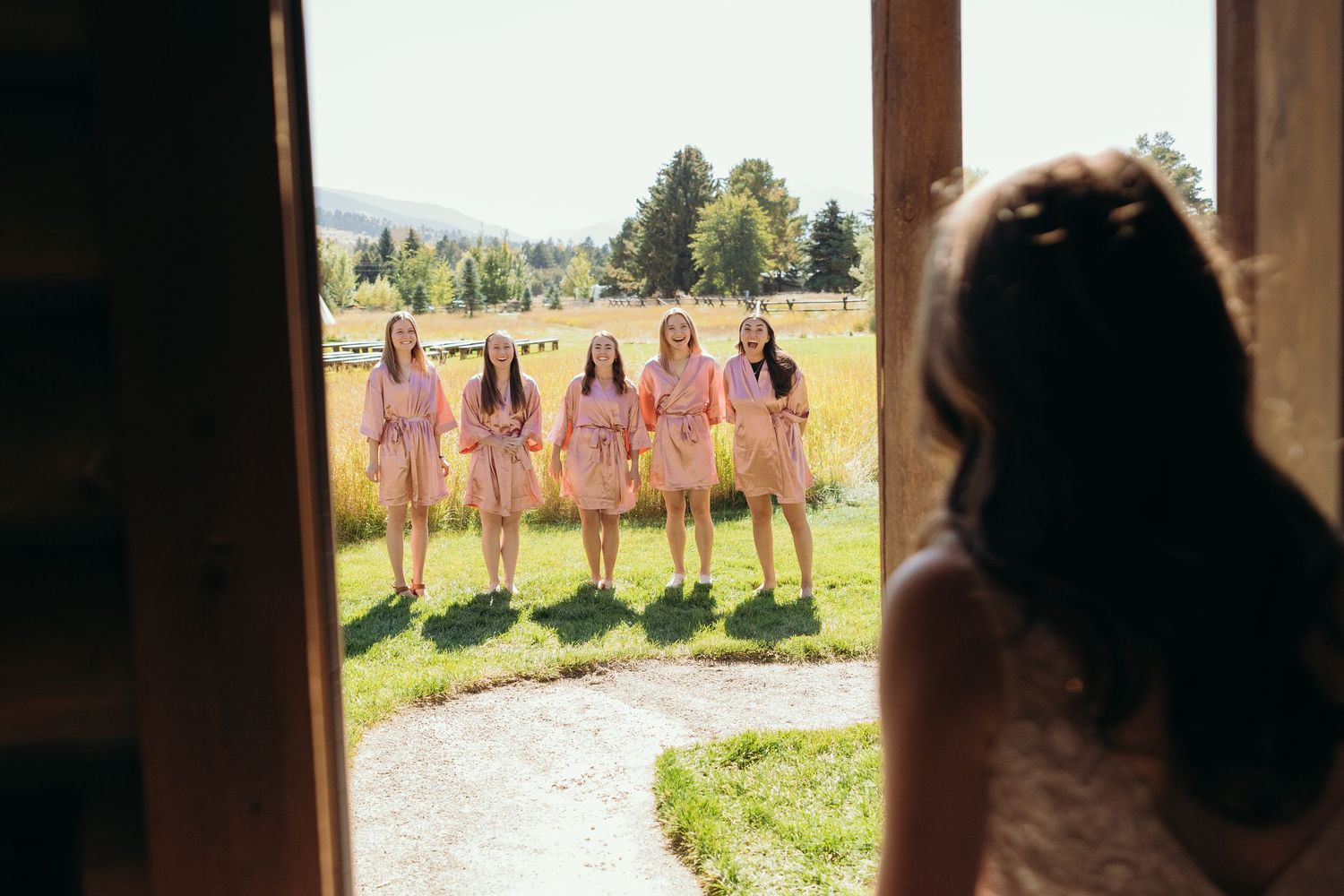 Wedding party poses in a line against a rustic outdoor backdrop during golden hour.