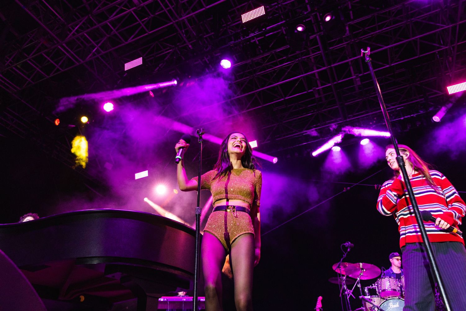 Rachel Zegler is performing on stage with vibrant purple lighting and stage effects.