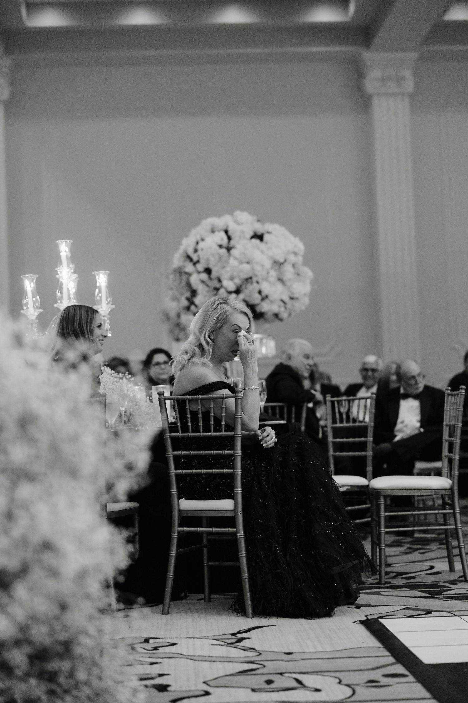 Black and white photo of an elegant wedding reception with floral centerpieces and chiavari chairs.