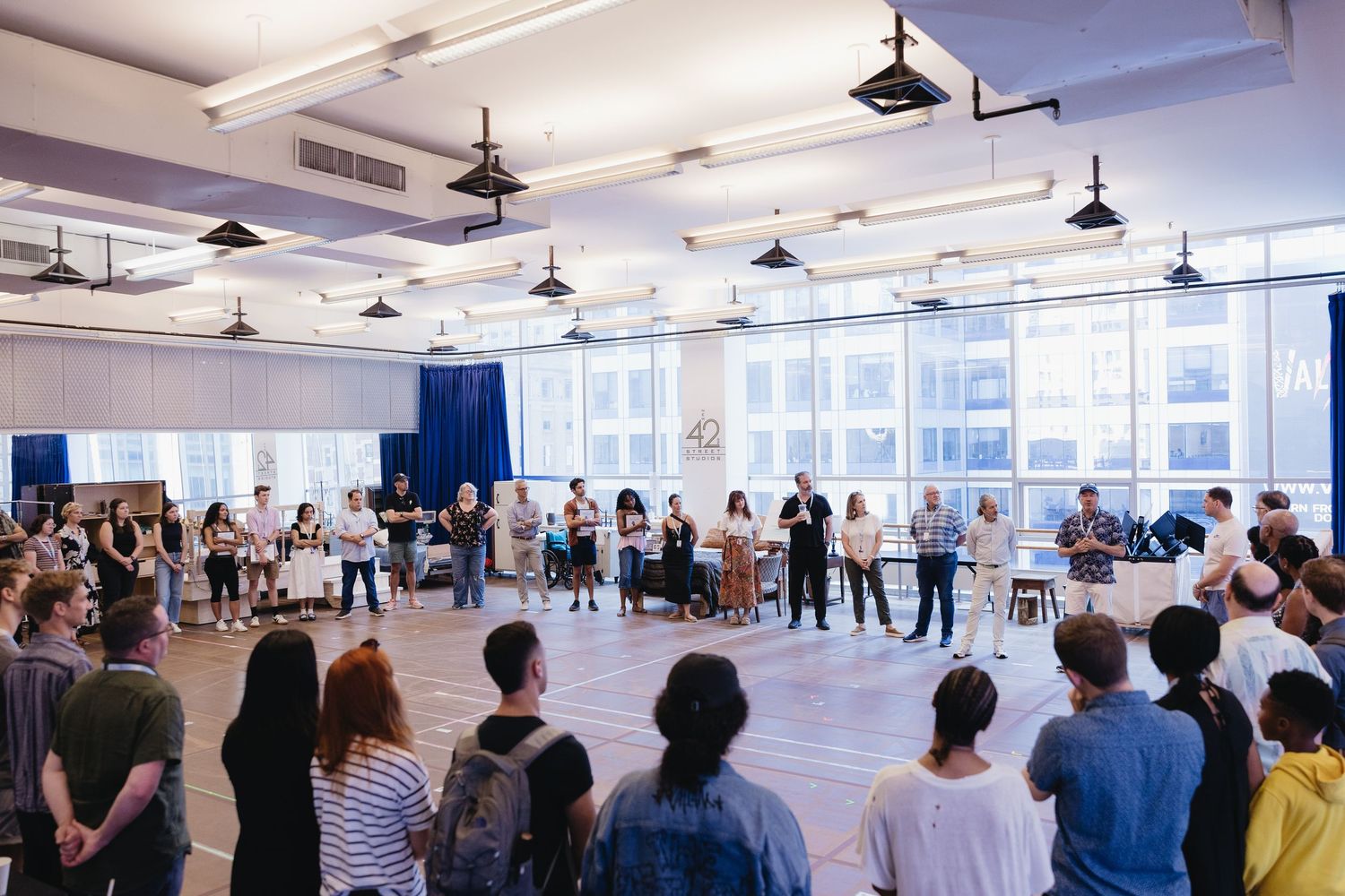 The notebook musical tour cast with large windows and pendant lights gathering for their first rehearsal