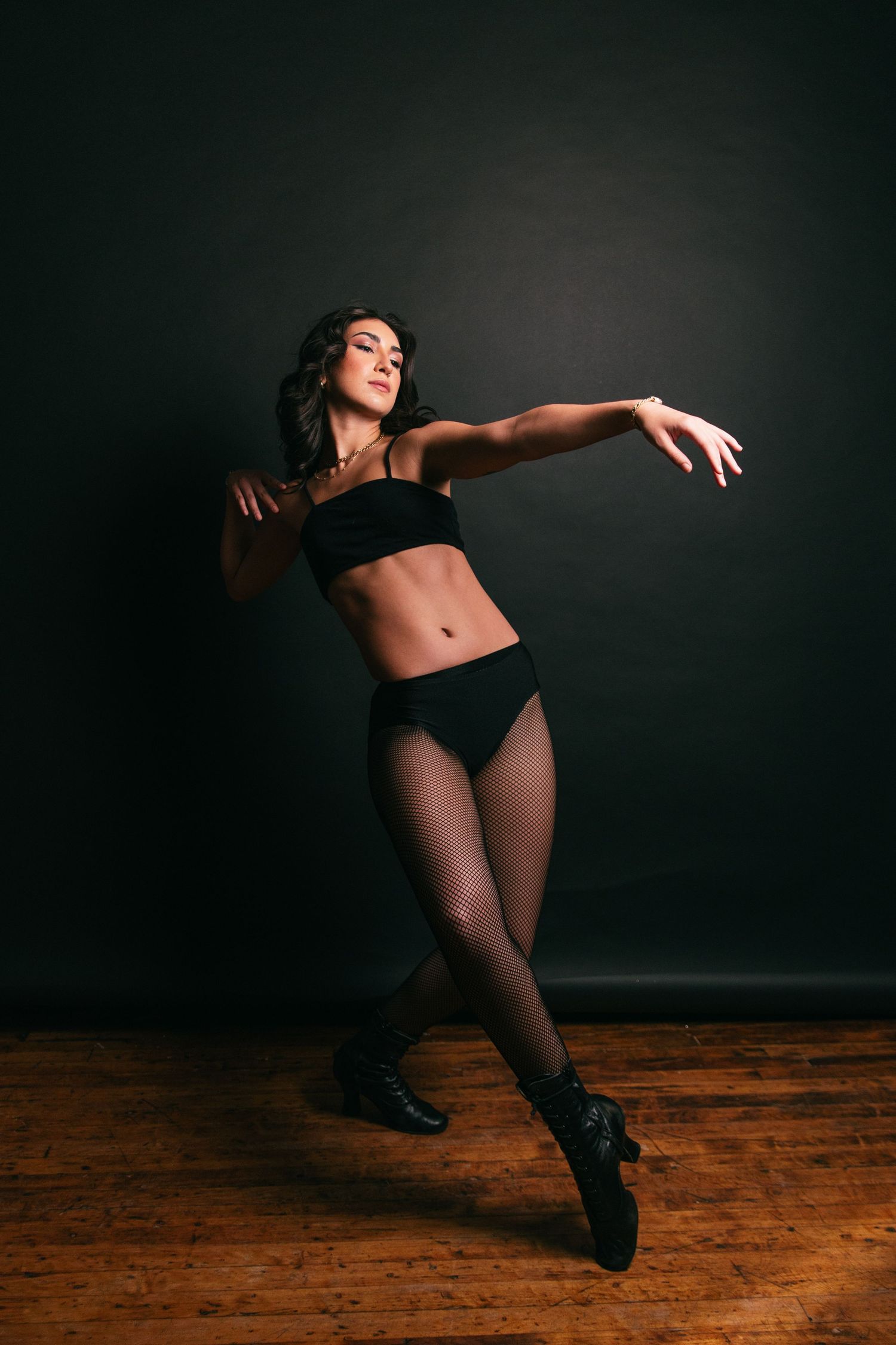 A dancer in black athletic wear performs a dynamic movement sequence on a wooden floor against a dark background.
