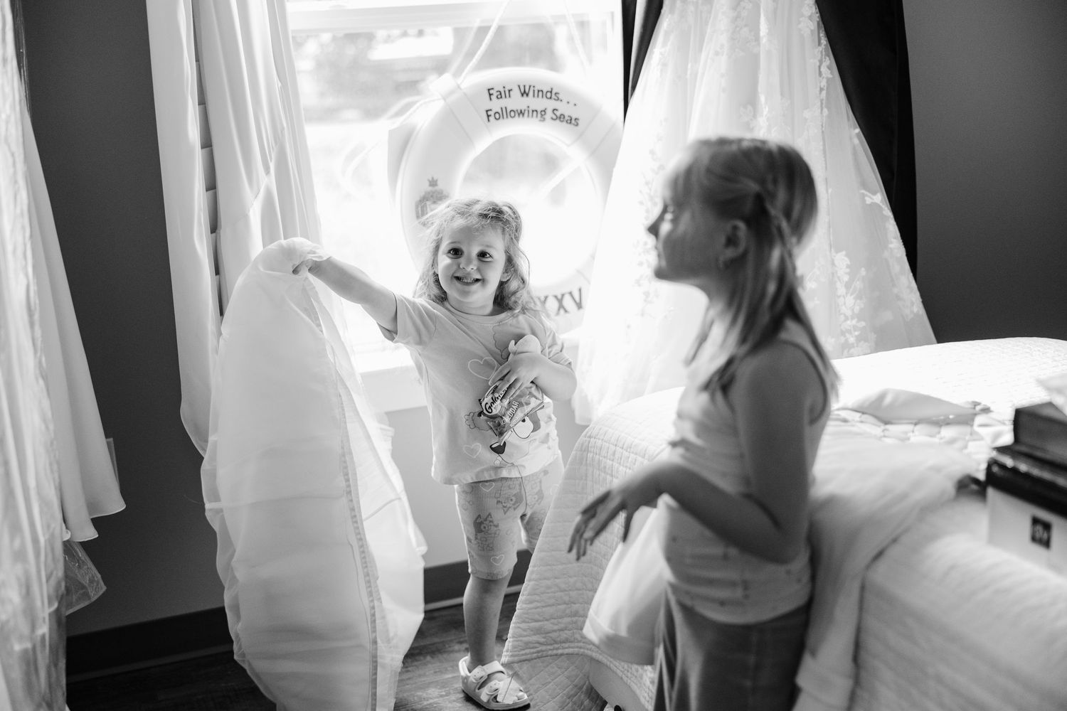 A black and white photo showing wedding dress preparations with curtains and gowns visible in the background.