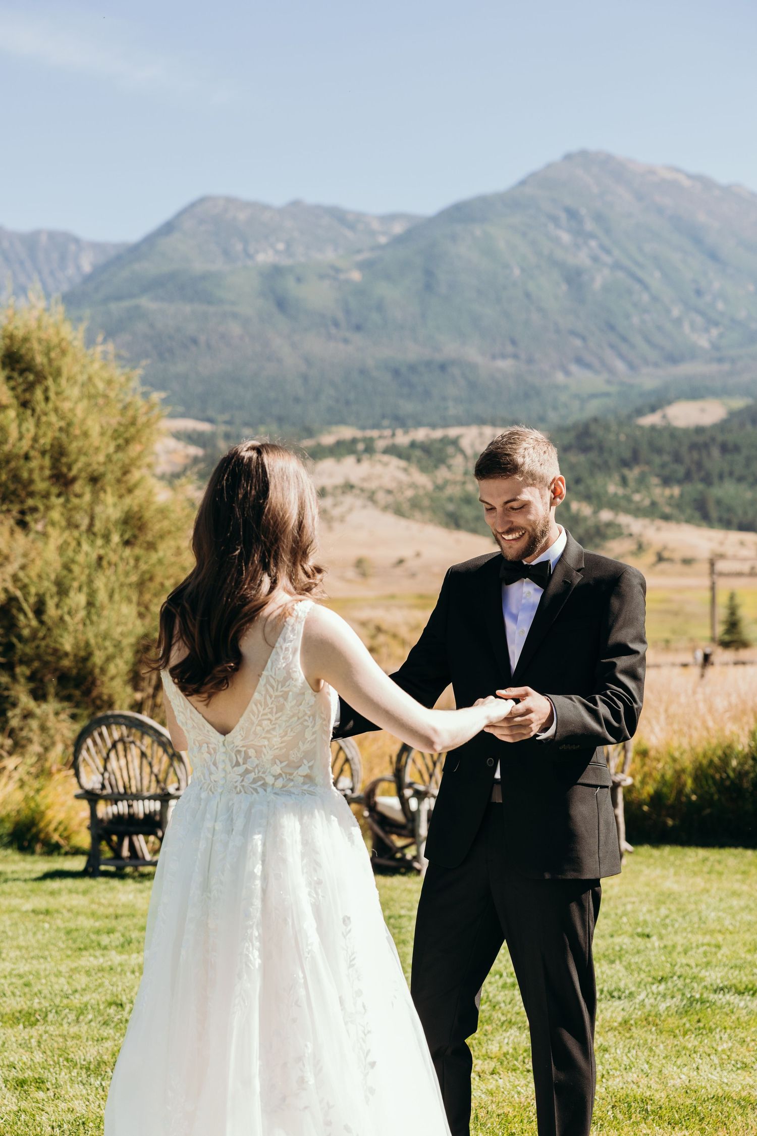 A couple laughs together during their first look moment with mountain scenery behind them.