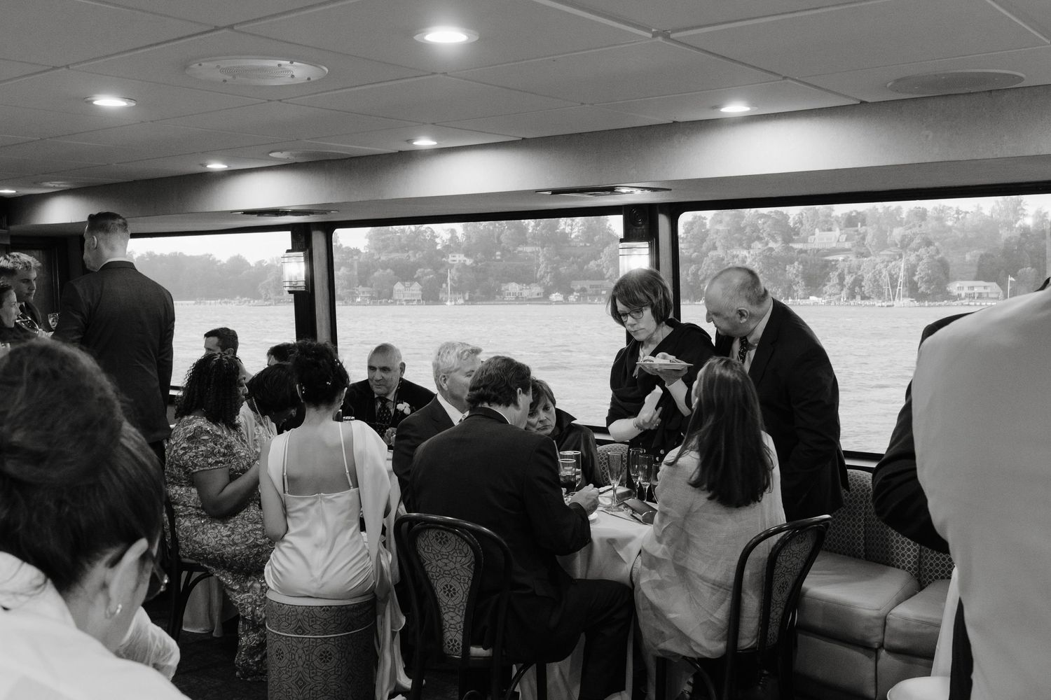 A panoramic view of wedding guests mingling in a reception venue with large windows.
