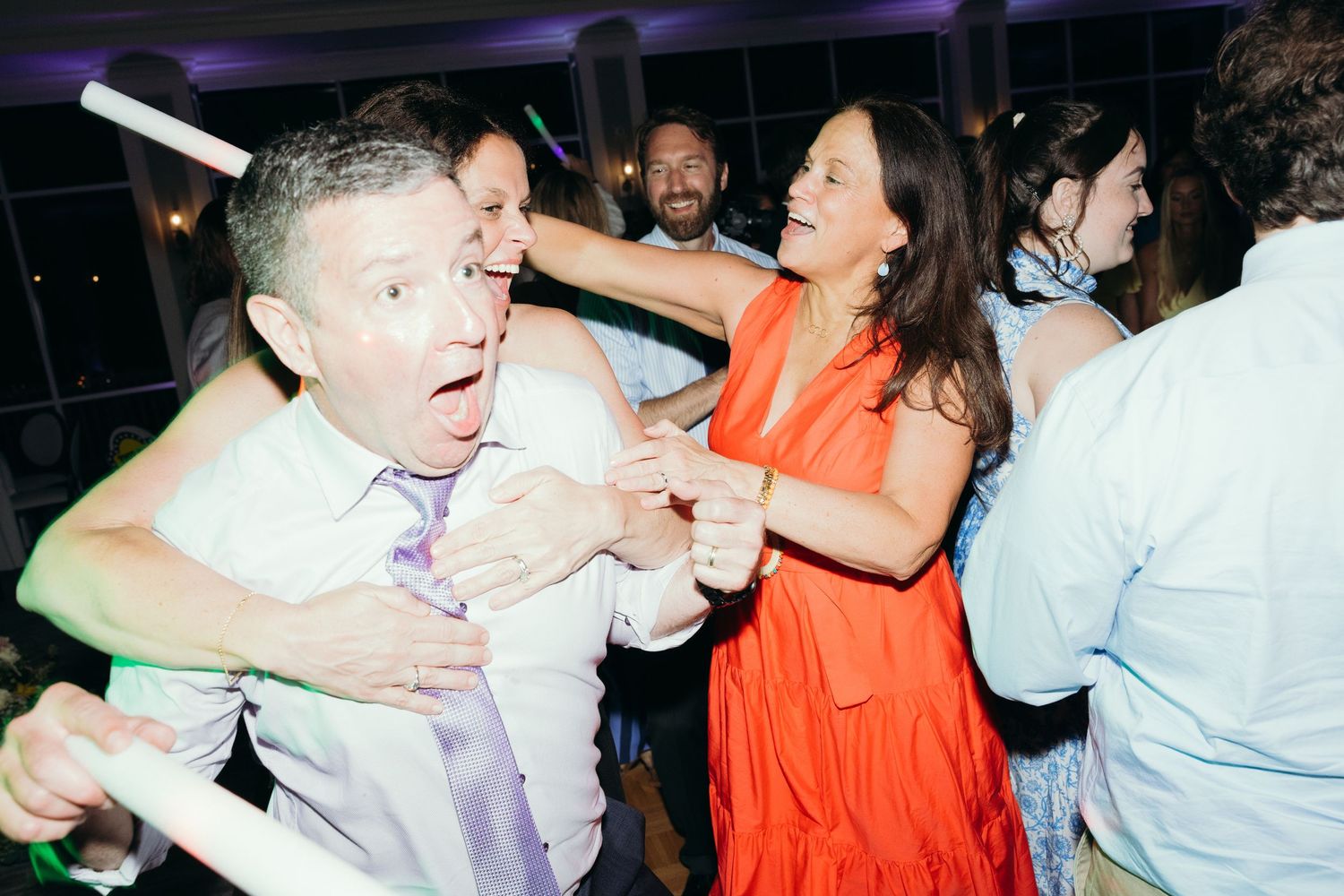 Wedding reception dance floor filled with guests dancing and celebrating under purple lighting.