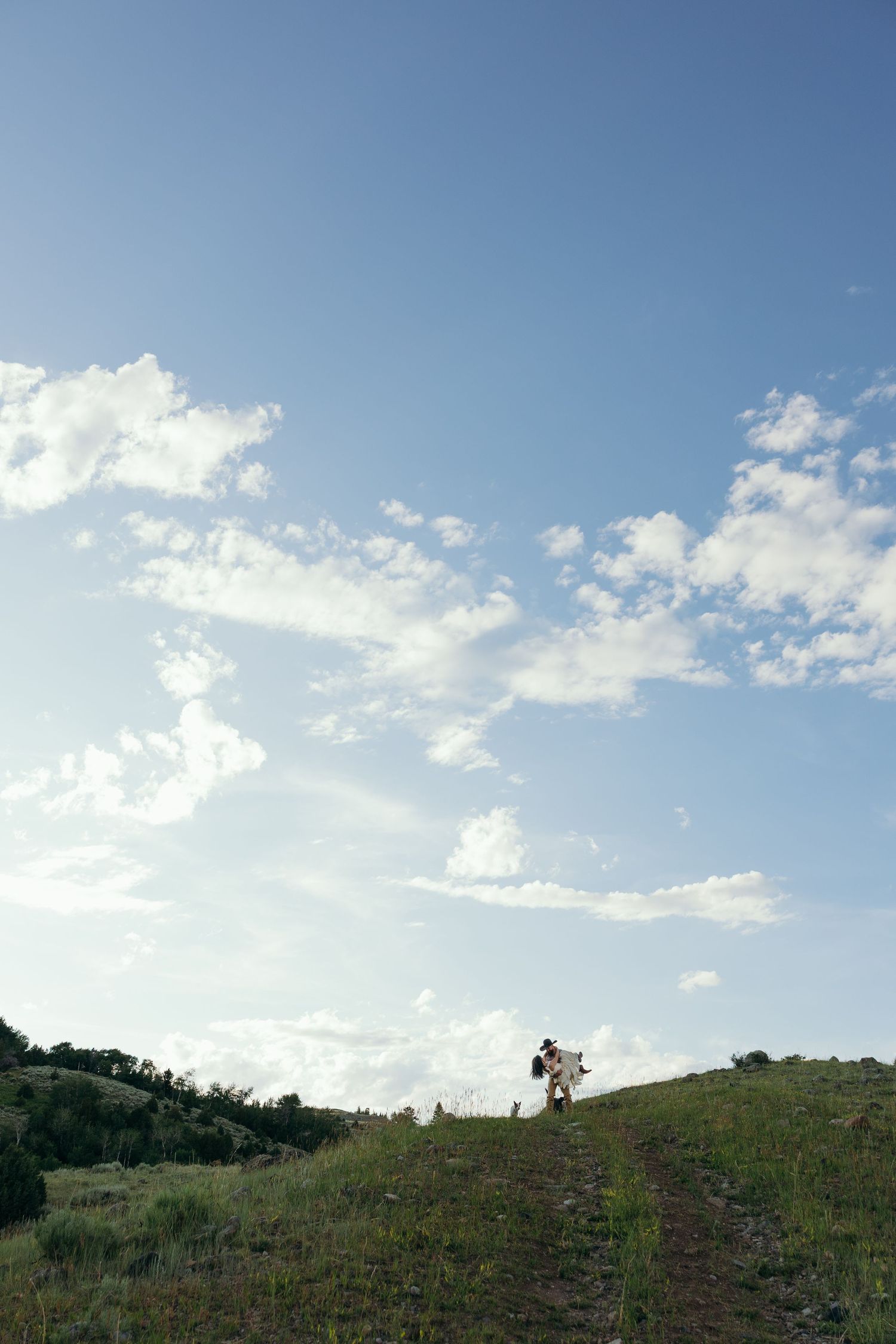 A distant silhouette of a couple standing on a hilltop against a bright blue sky.