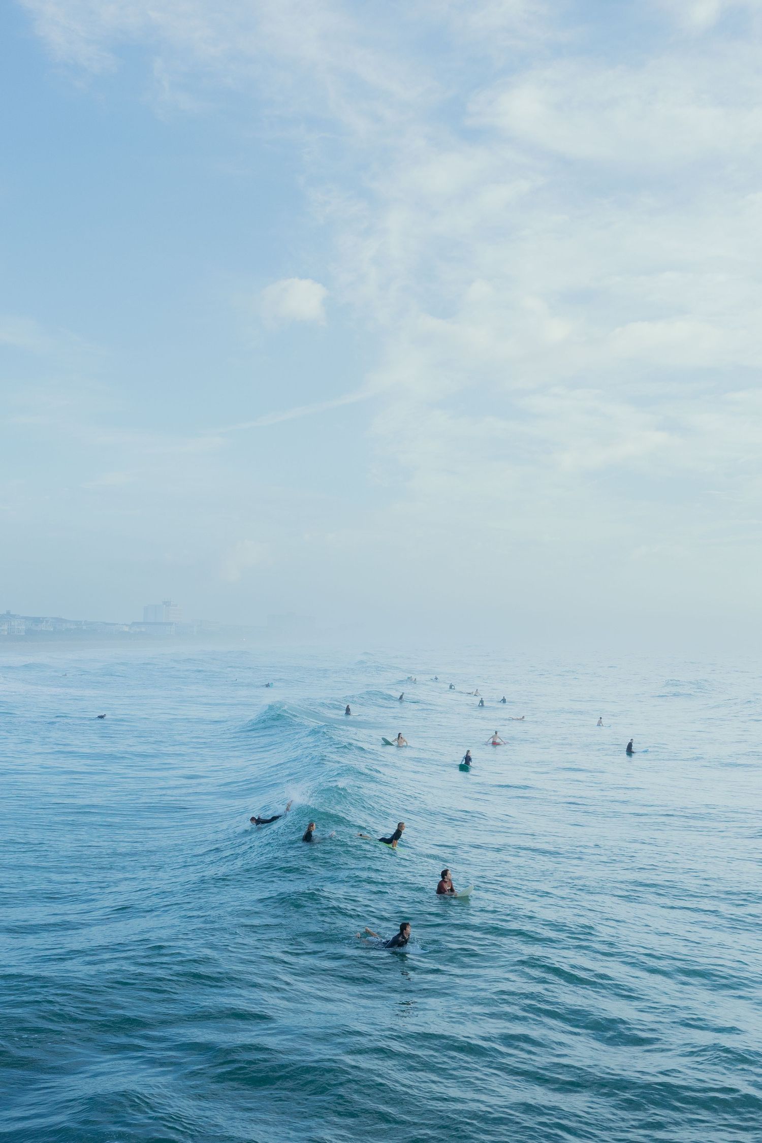 Surfers riding gentle waves in a serene blue ocean under a cloudy sky.