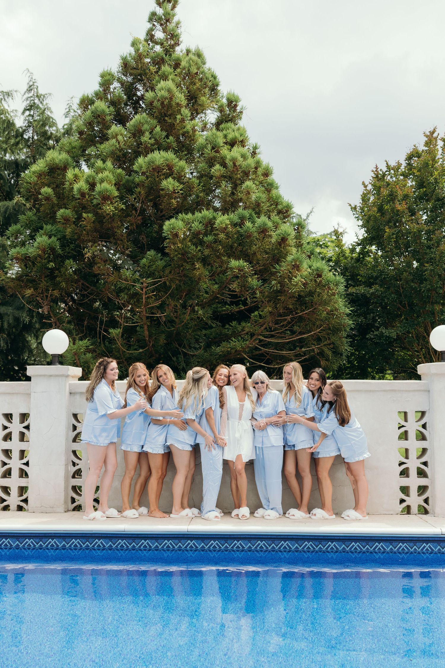 Bridesmaids in light blue dresses posing together by a swimming pool.