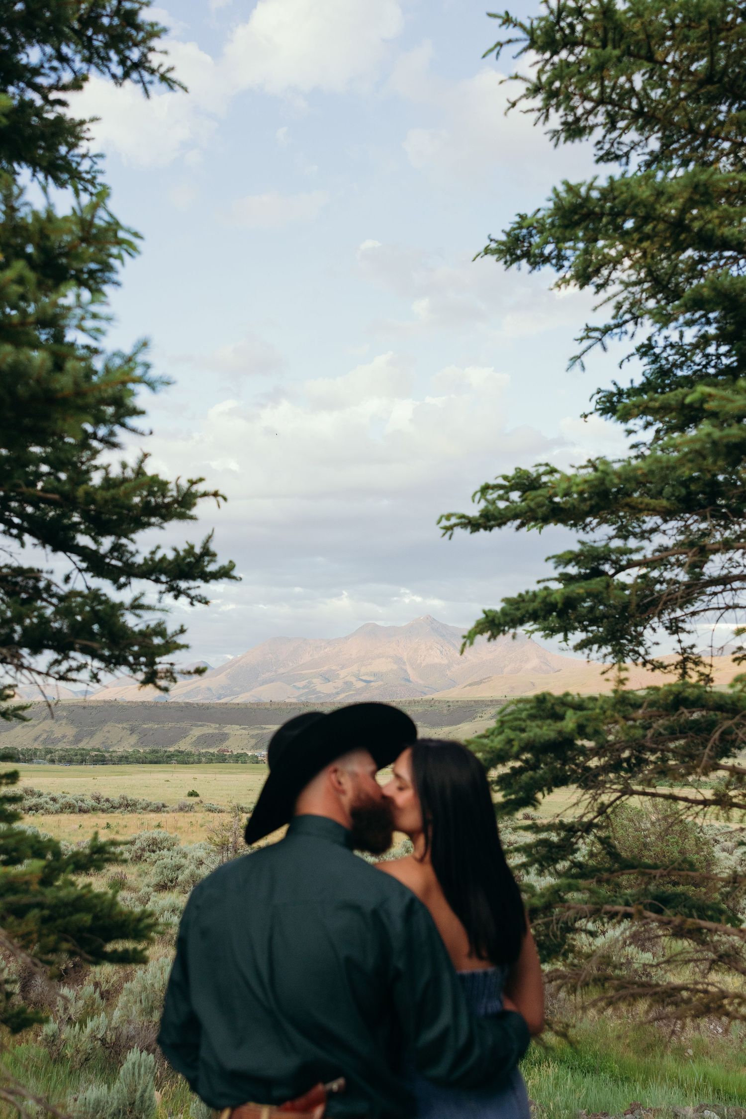A tender moment captured between a couple against a mountainous backdrop with trees.