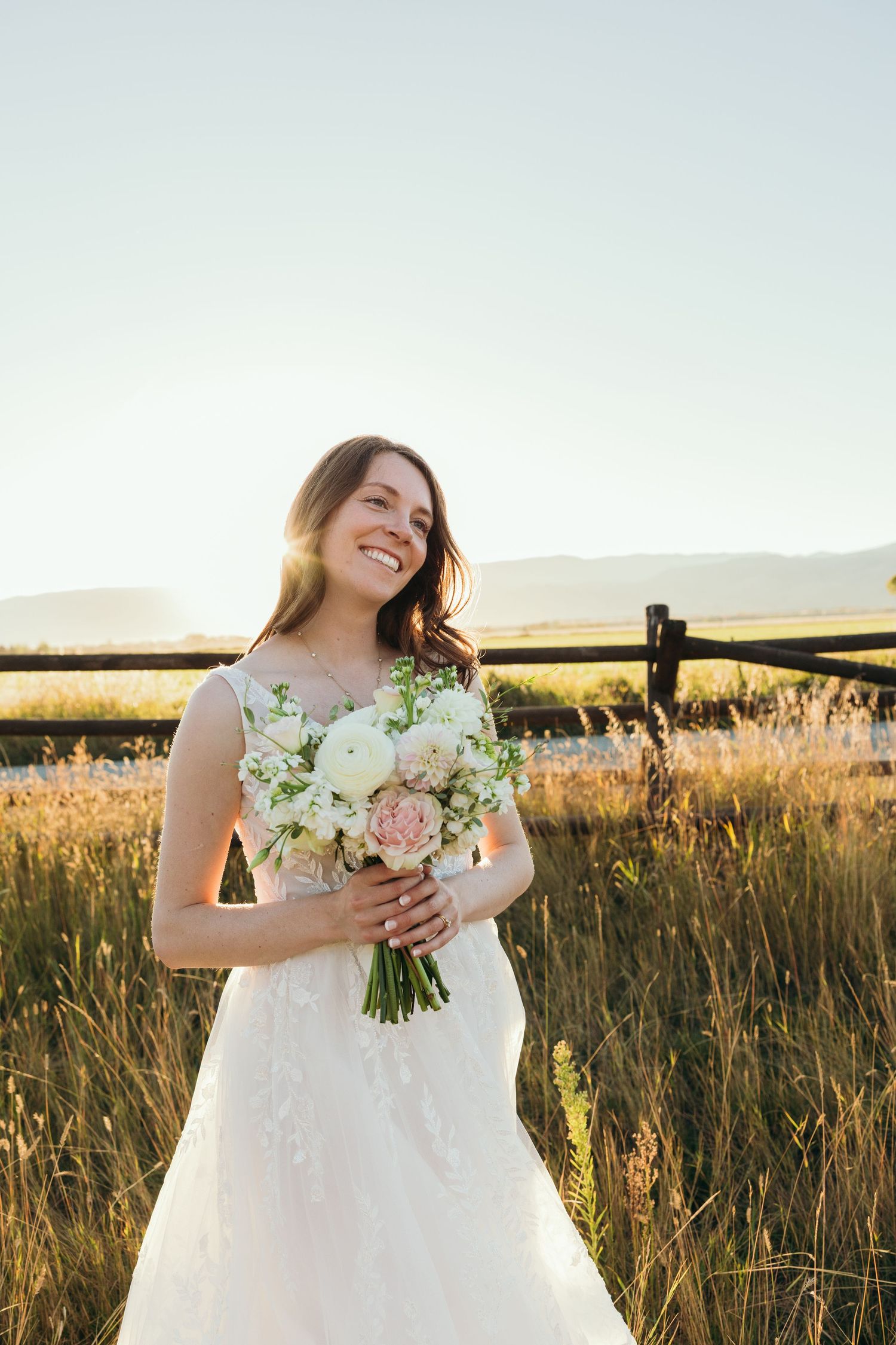 Bride in white dress holding bouquet in golden sunset field.