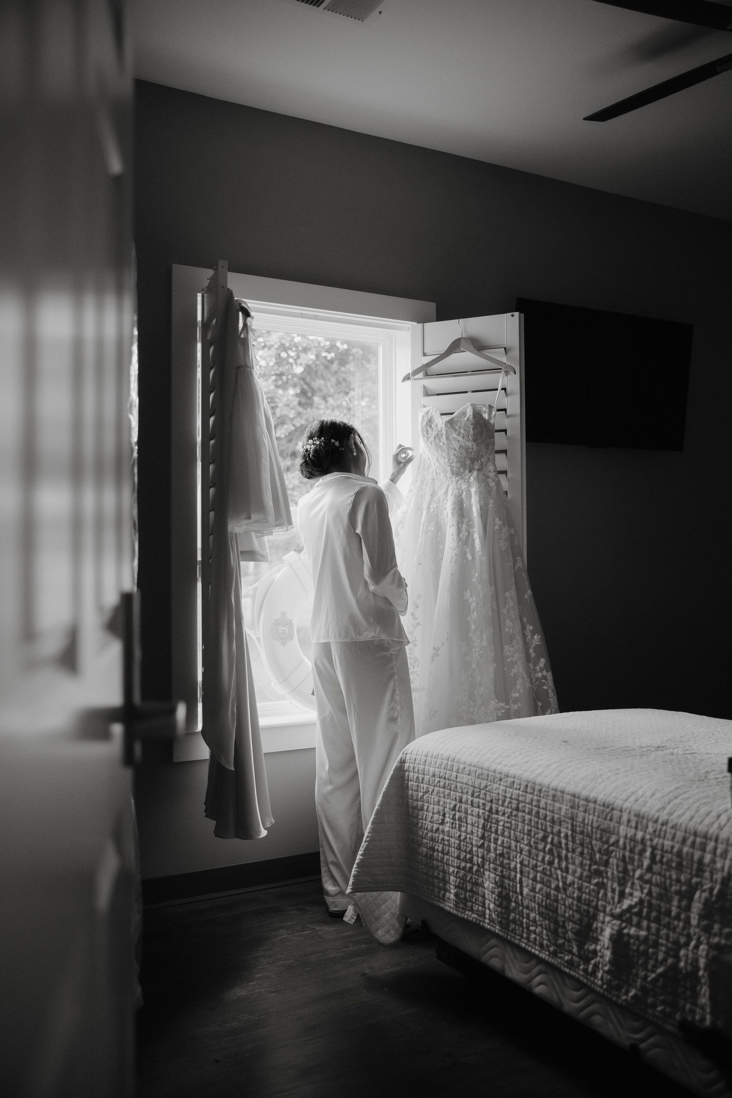 A wedding dress hangs by a window in a dimly lit room.