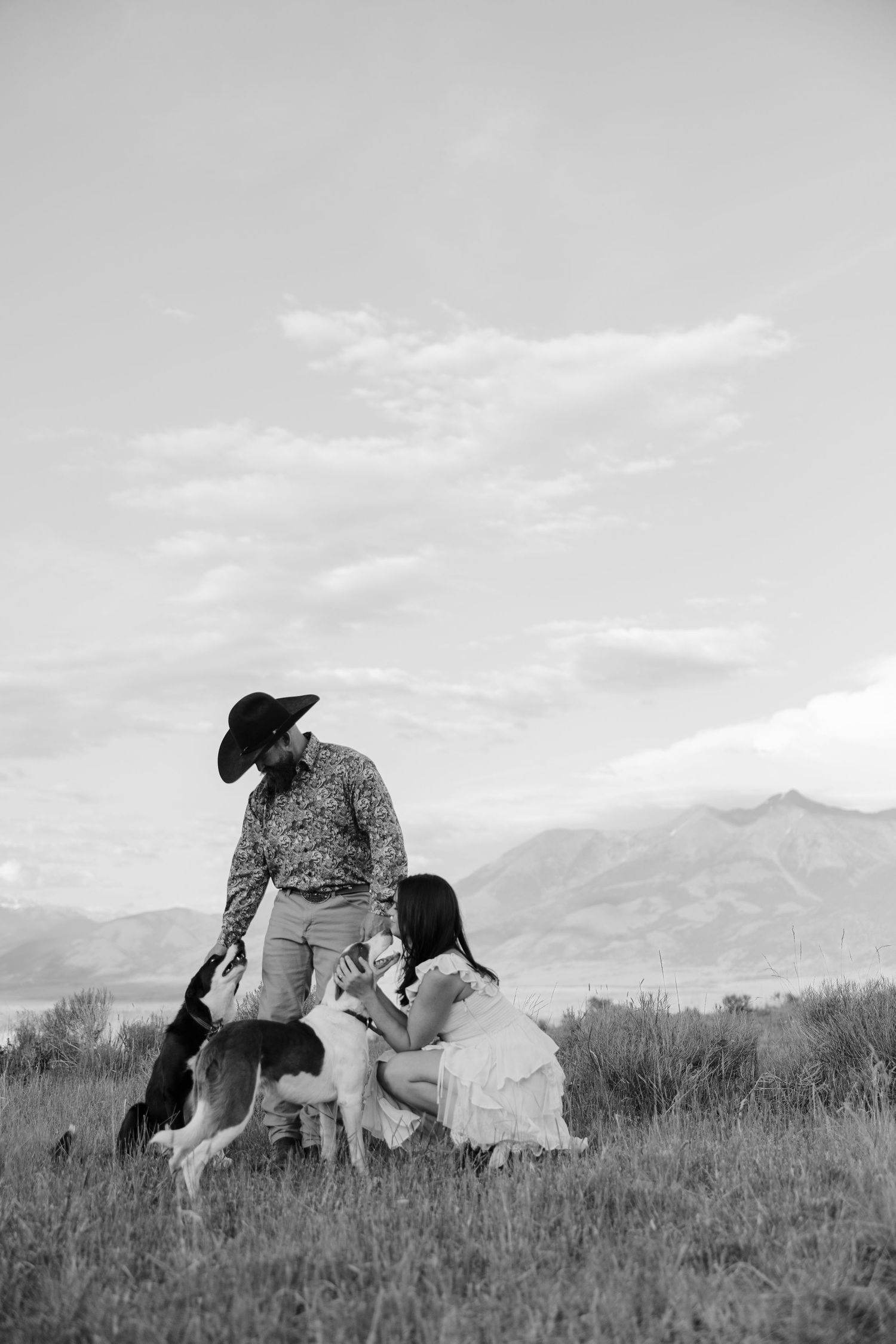 Black and white photo of people playing and running in a grassy field with mountains in background.