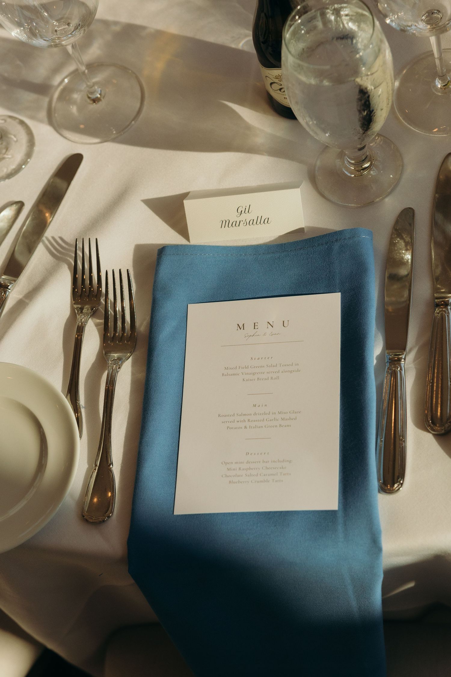 Wedding place settings with blue napkins and printed menus on white tablecloths.