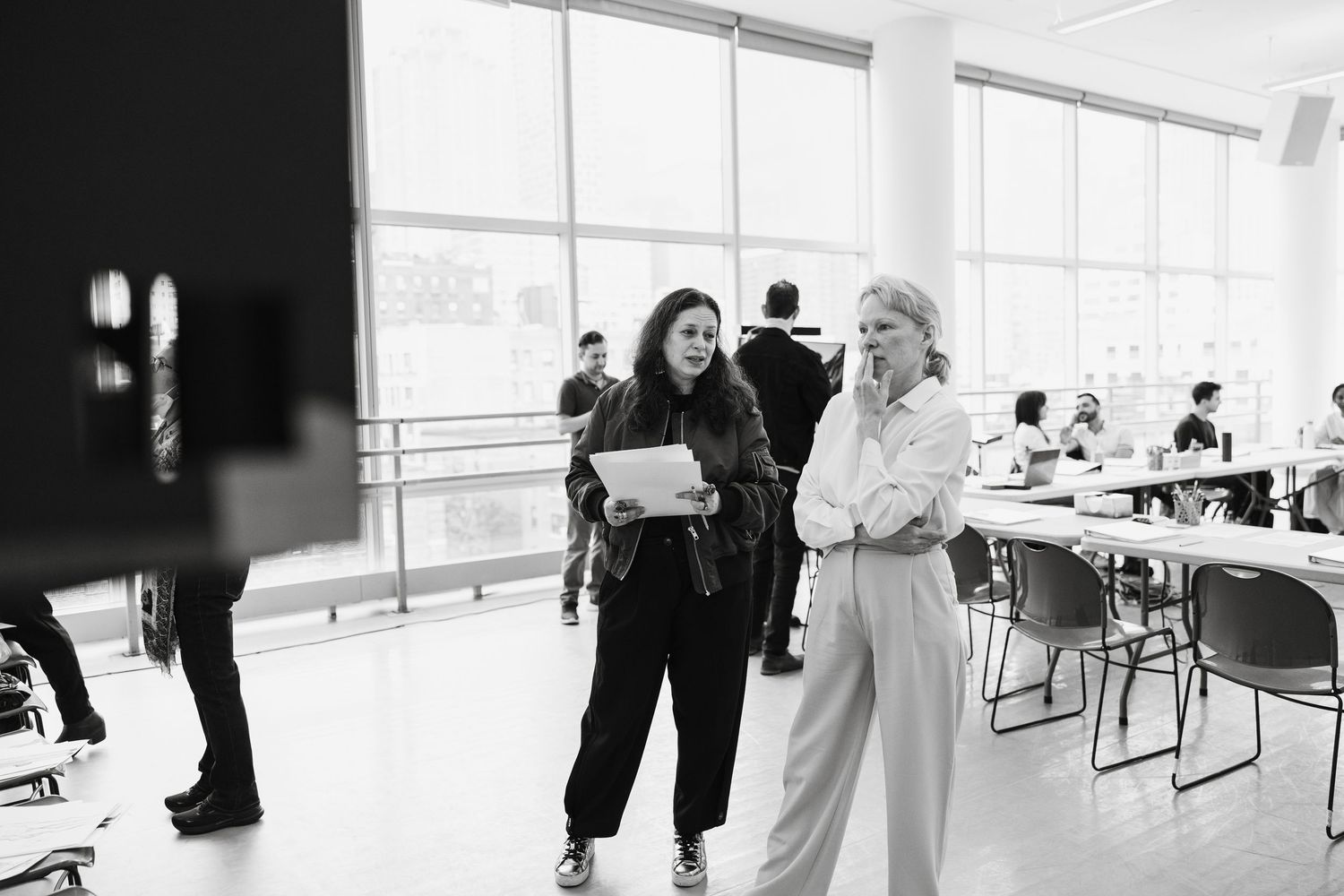 Black and white photo of Pamela Anderson and Costume Department of Williamstown theater festivagathered in bright studio space with windows.