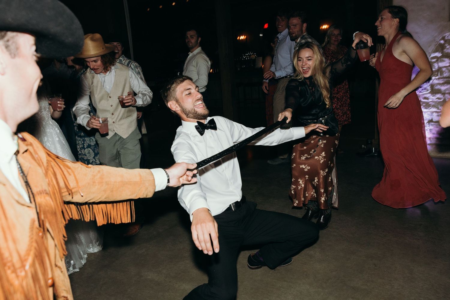 Wedding guests dancing and celebrating in a dimly lit rustic venue.